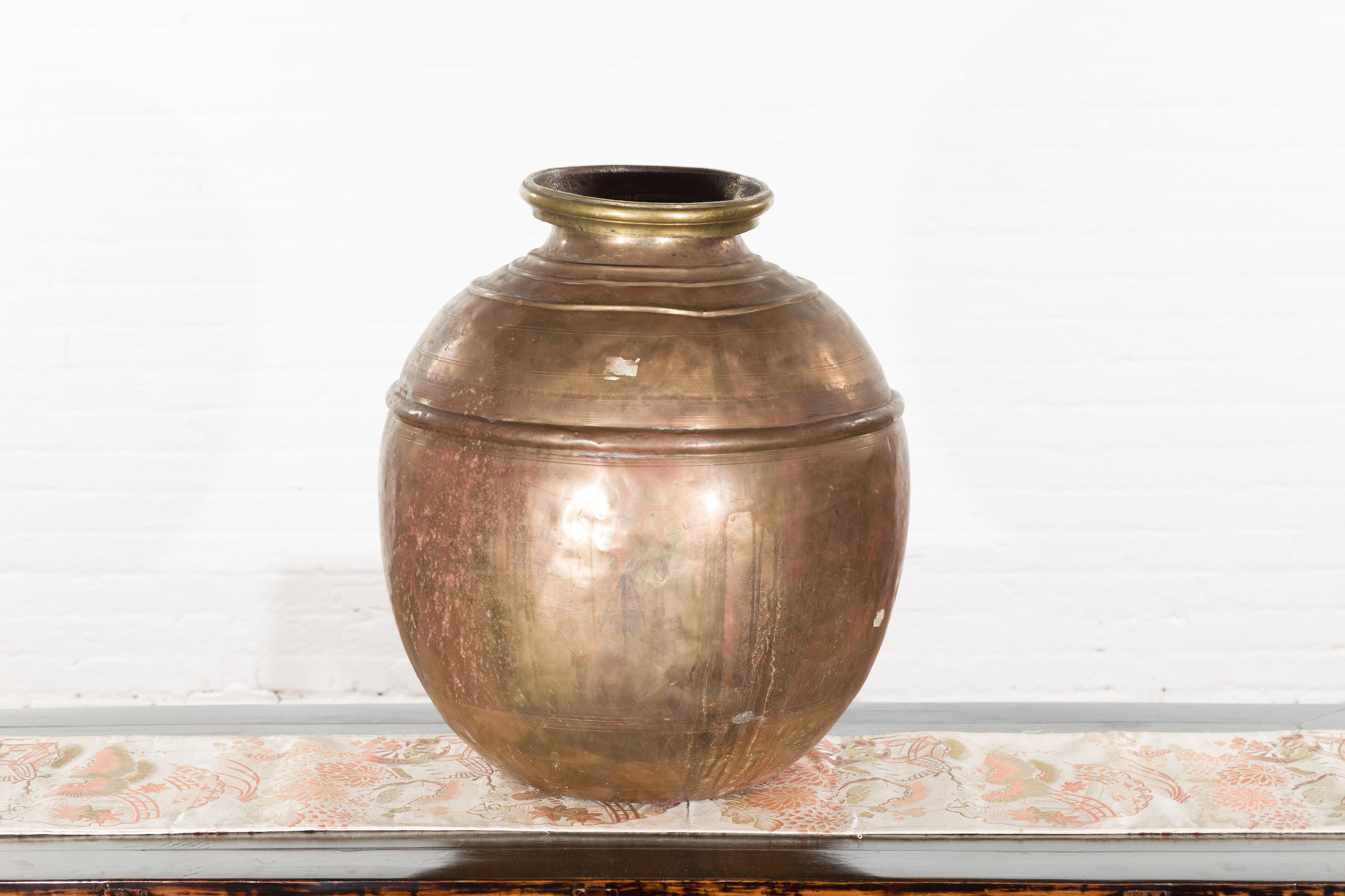 An Indian vintage brass water jar from the mid 20th century, with distressed appearance. Created in India during the midcentury period, this brass water jar features a generous circular body with concentric motifs, topped with a large lip. Boasting