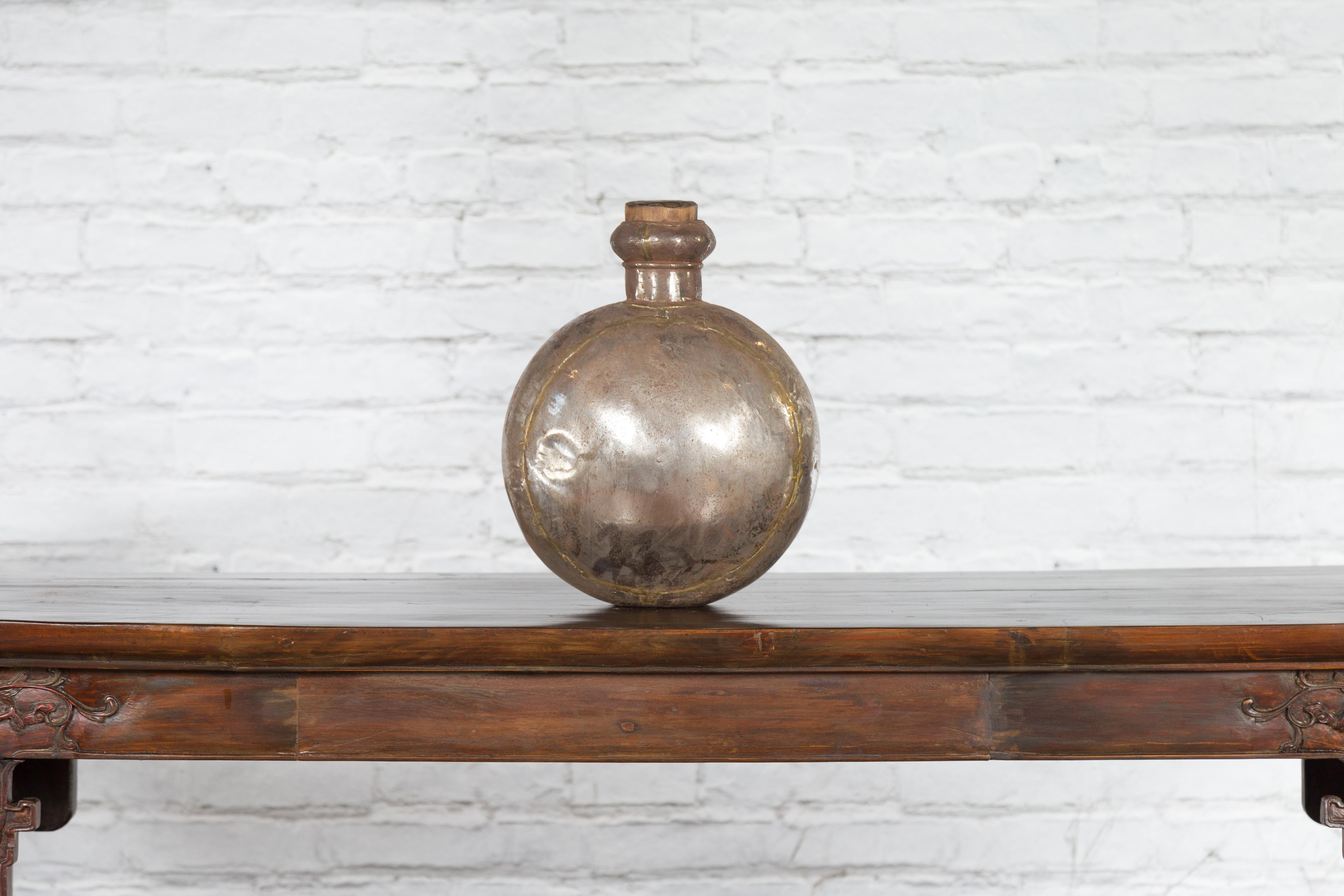 A vintage Indian metal water vase from the mid-20th century, with circular belly and cork inspired wooden top. Crafted in India during the midcentury period, this metal water vase charms our eyes with its round silhouette lines and nicely weathered