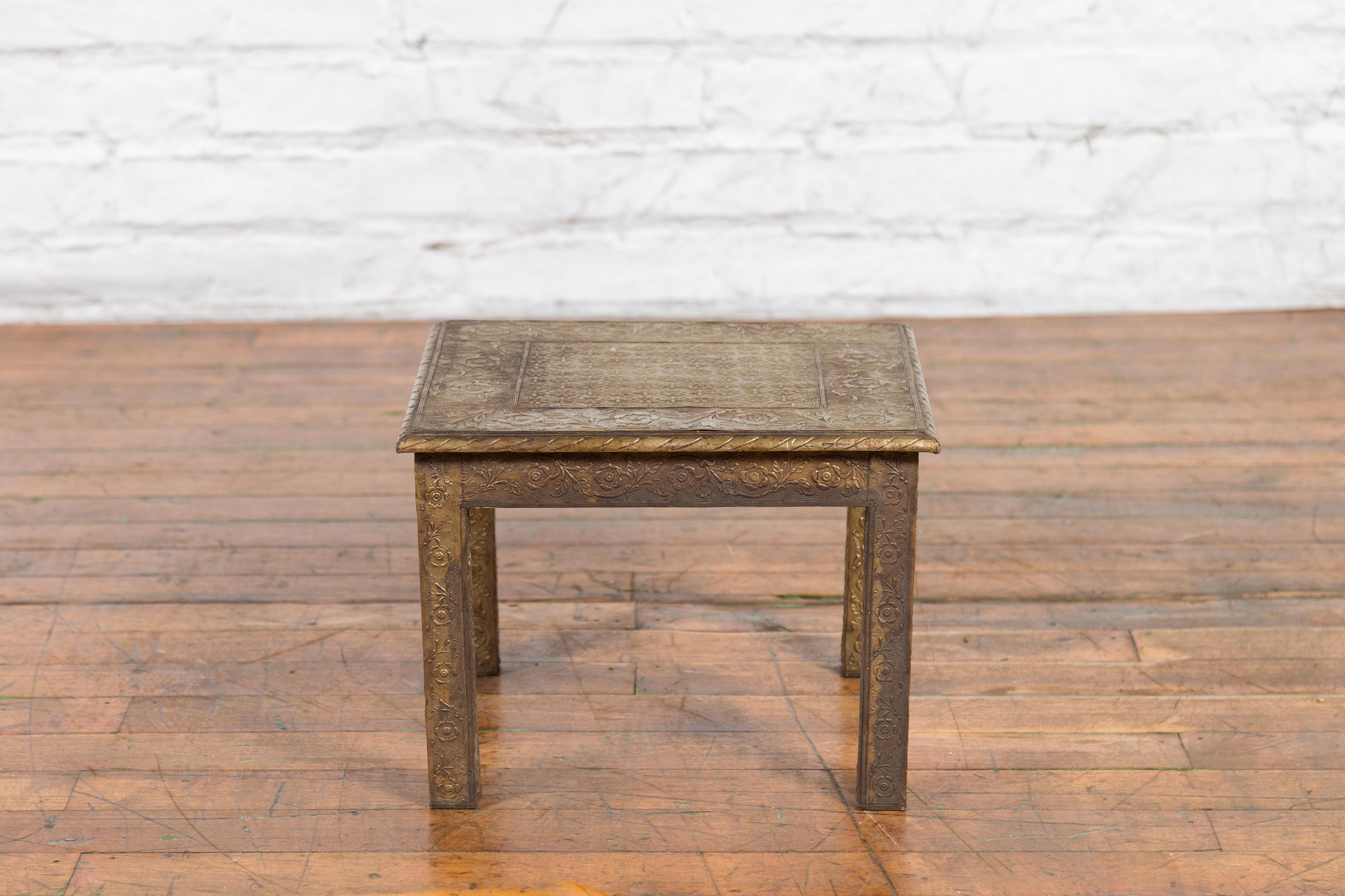 A vintage square-shaped Indian side table from the mid 20th century, with repoussé motifs. Created in India during the midcentury period, this side table features a square shaped top adorned with a repoussé floral frieze surrounding petite rosettes.