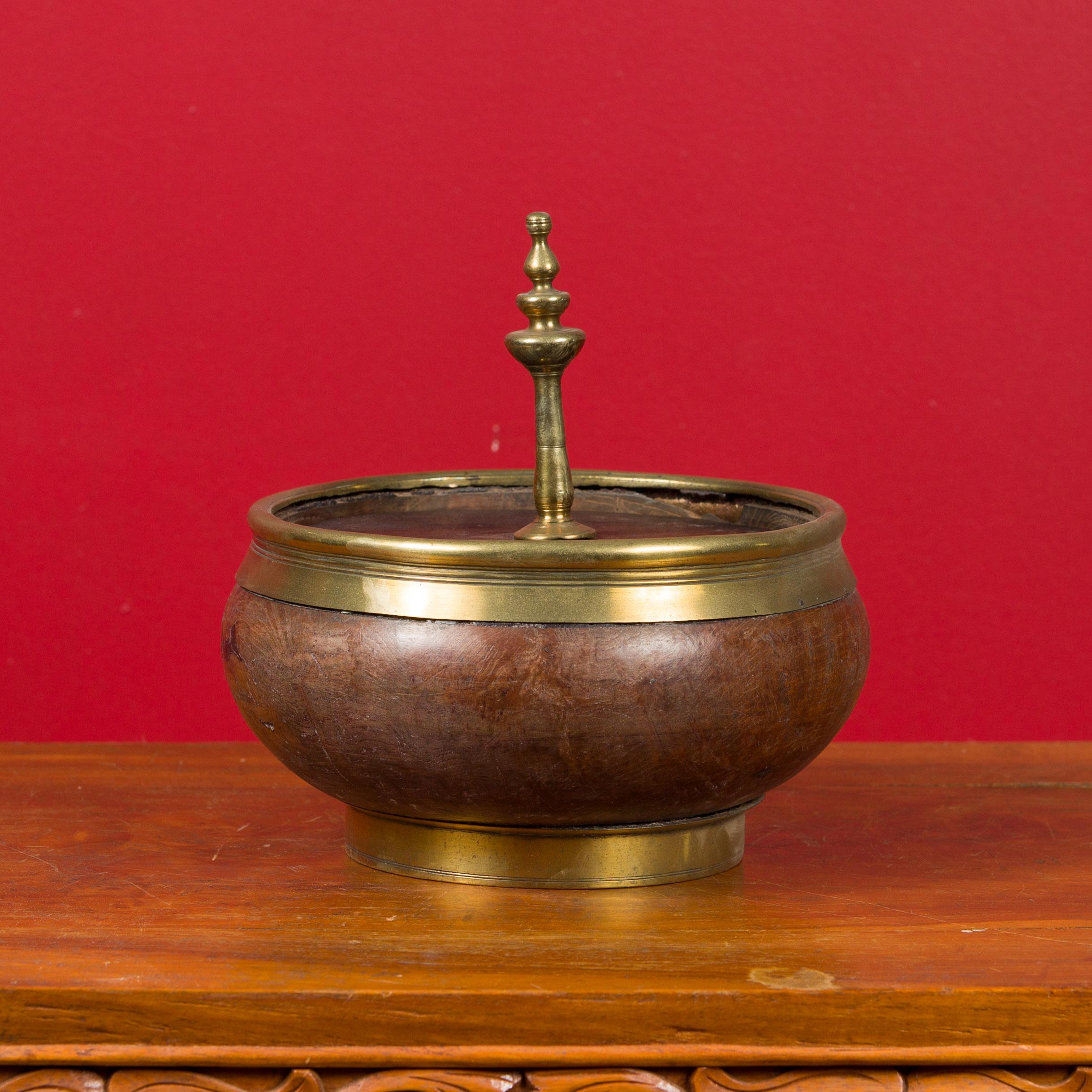 An Indian vintage wood and brass lidded bowl from the mid-20th century, with central finial. Created in India during the midcentury period, this small lidded bowl features a circular silhouette showcasing a nice contrast of colors between the dark