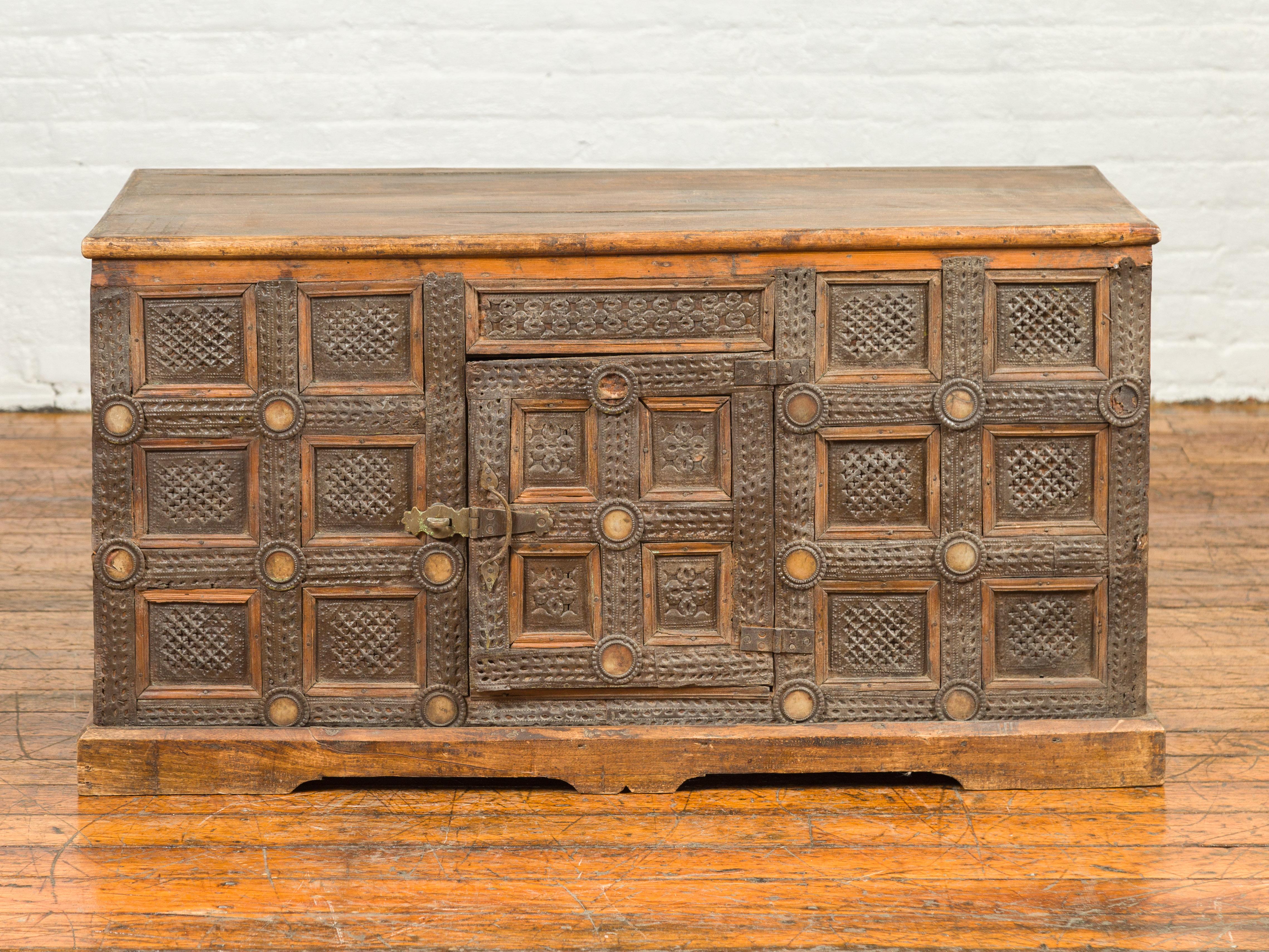 A vintage Indian wood and metal cabinet from the mid-20th century, with geometric decor. Born in India during the midcentury period, this cabinet attracts our attention with its richly decorated façade and weathered appearance. The cabinet is