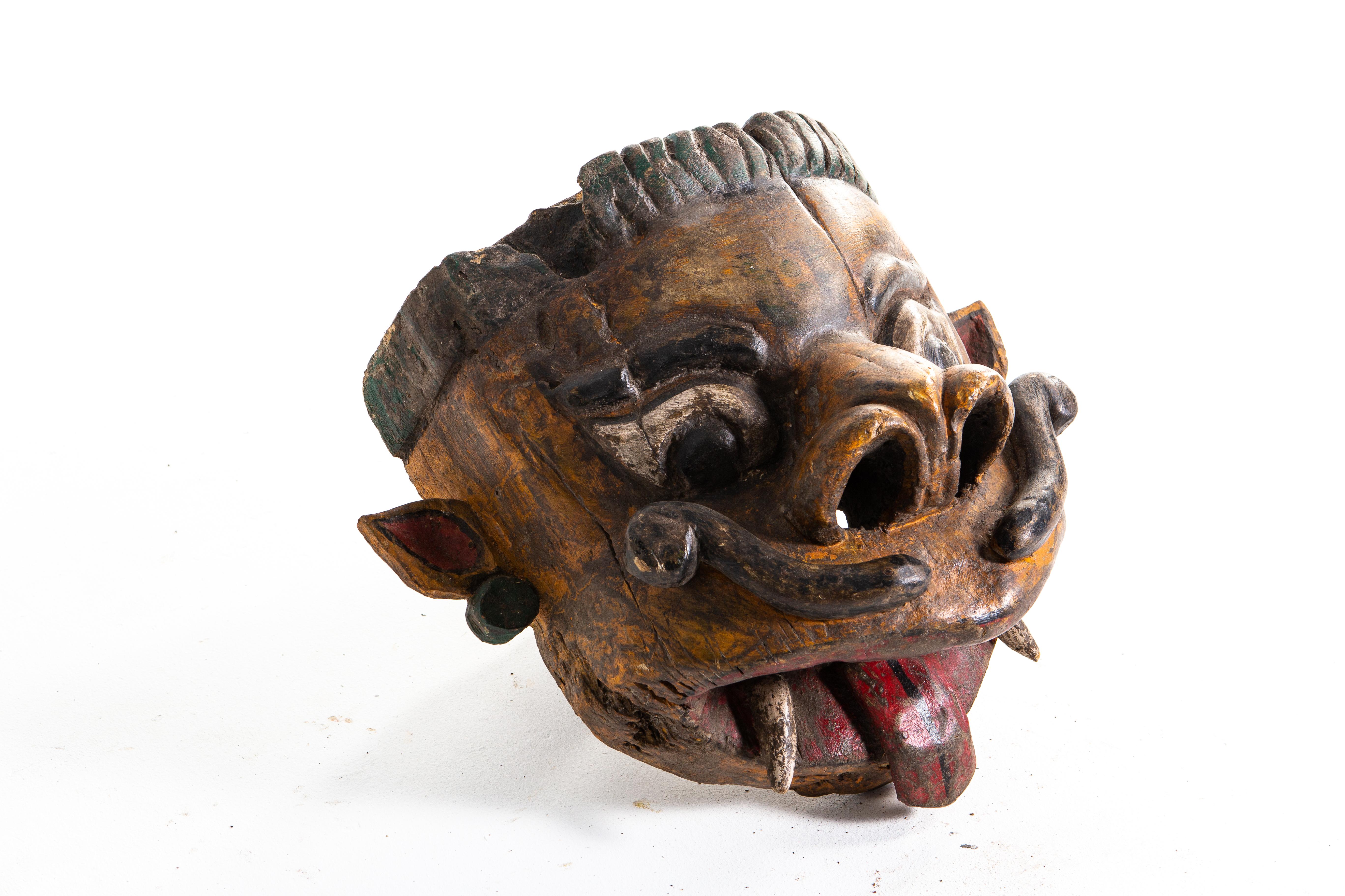 Poly-chrome wooden mask from Rajasthan, India, made from Sheesham wood, circa 20th century. The mask features a grotesque smile that is designed to ward off the evil eye. According to traditional beliefs, a beautiful mask would only lure envy and