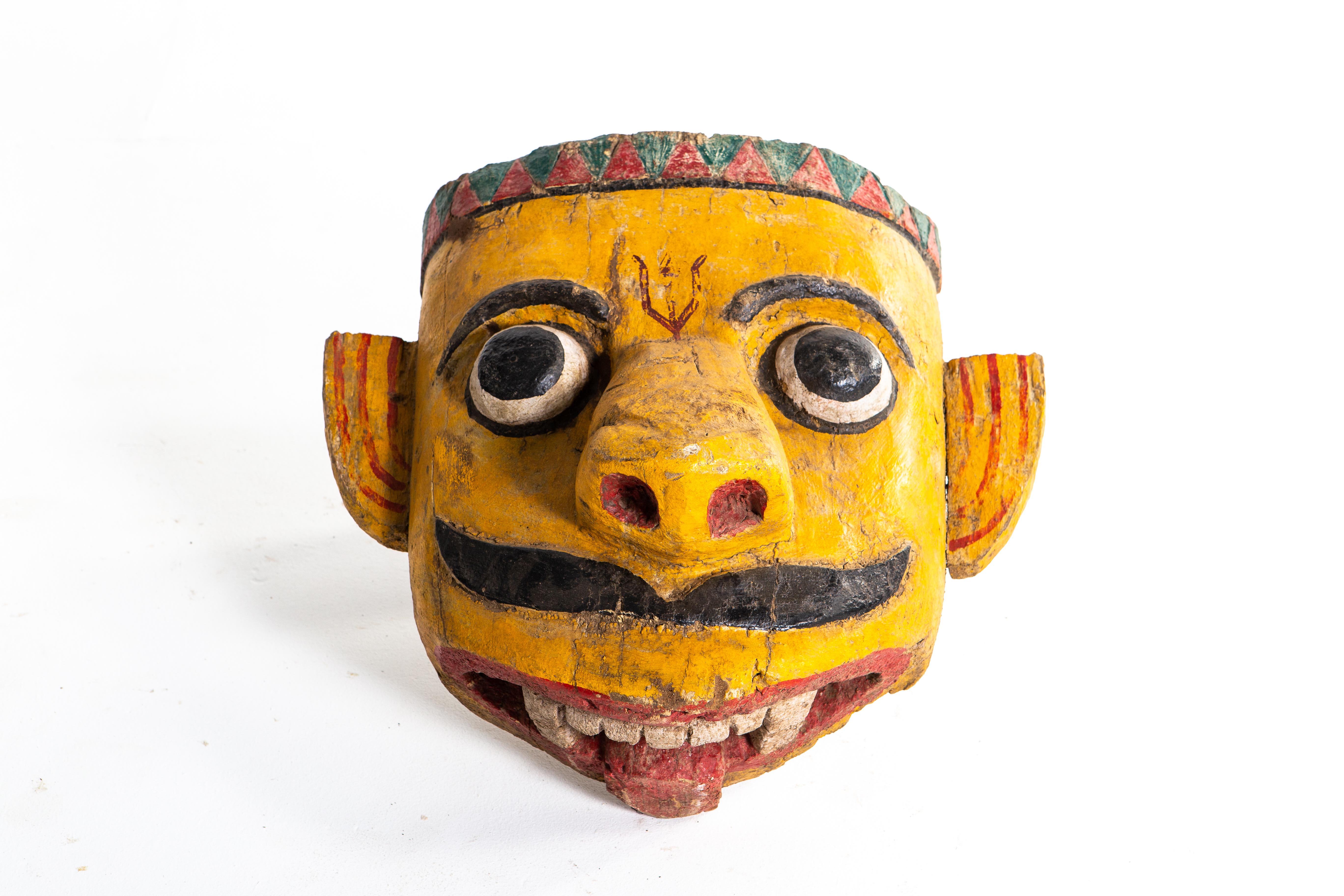 Poly-chrome wooden mask from Rajasthan, India, made from sheesham wood, circa 20th century. The mask features a grotesque smile that is designed to ward off the evil eye. According to traditional beliefs, a beautiful mask would only lure envy and