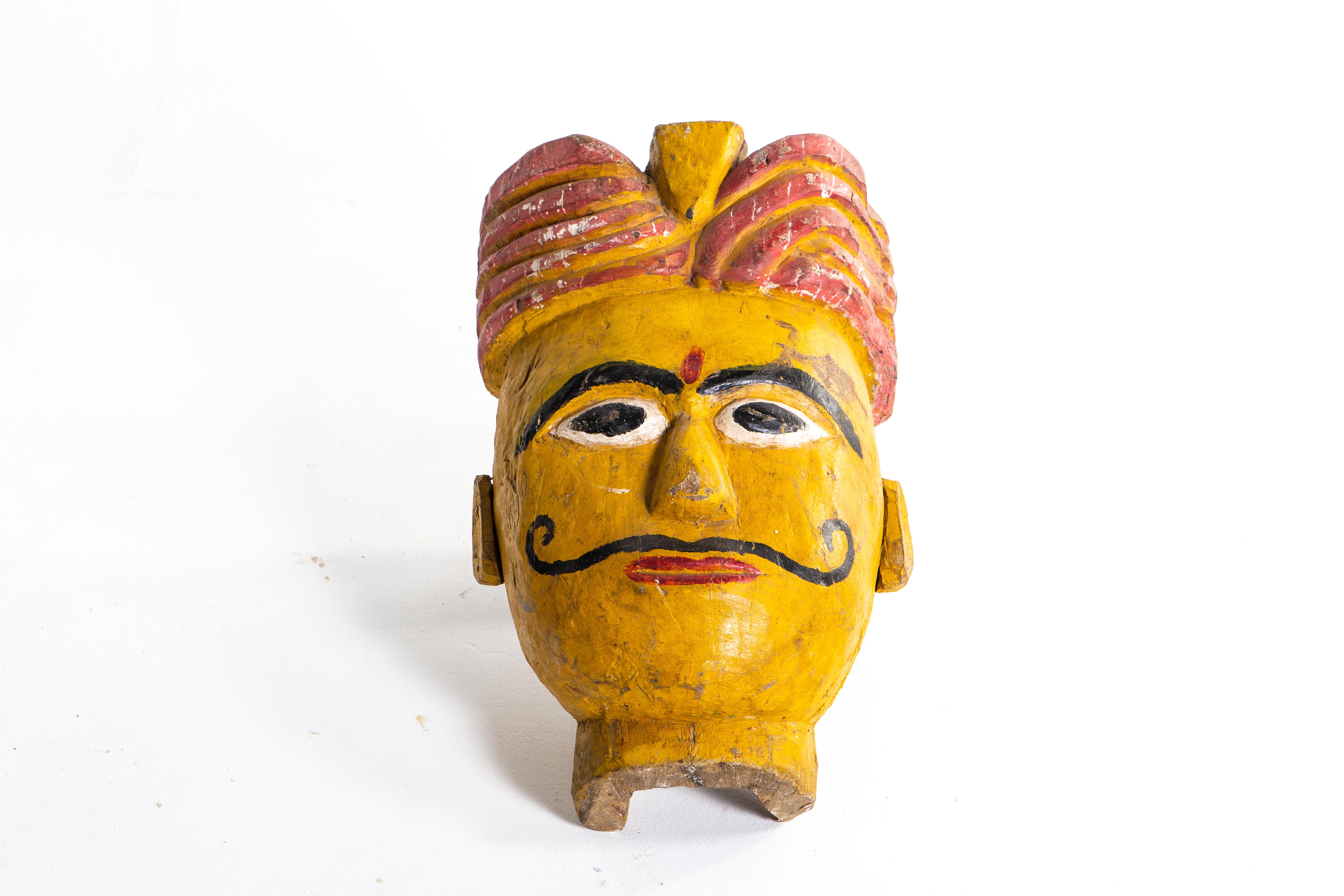 Poly-chrome wooden mask from Rajasthan, India, made from sheesham wood, circa 20th century. The mask features a grotesque smile that is designed to ward off the evil eye. According to traditional beliefs, a beautiful mask would only lure envy and