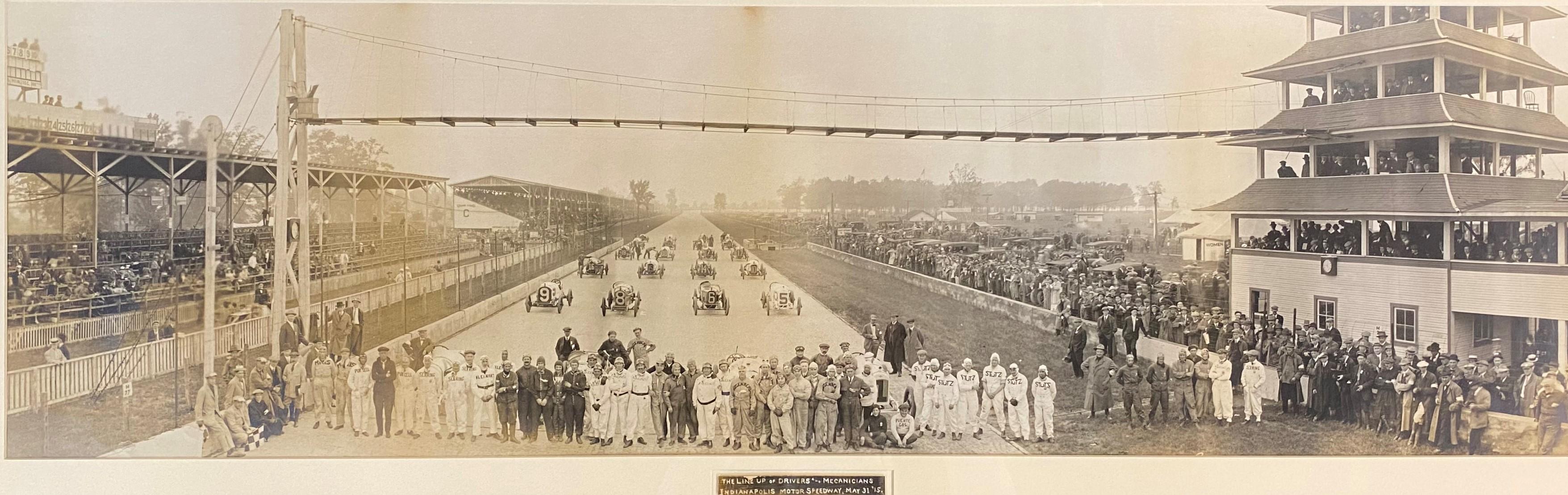 A wonderful panoramic sepia photograph of the Indy 500 racing drivers, cars, & mechanics on the raceway of the Indianapolis Motor Speedway, with a caption below which reads “The Lineup of Drivers and Mechanicians, Indianapolis Motor Speedway, May