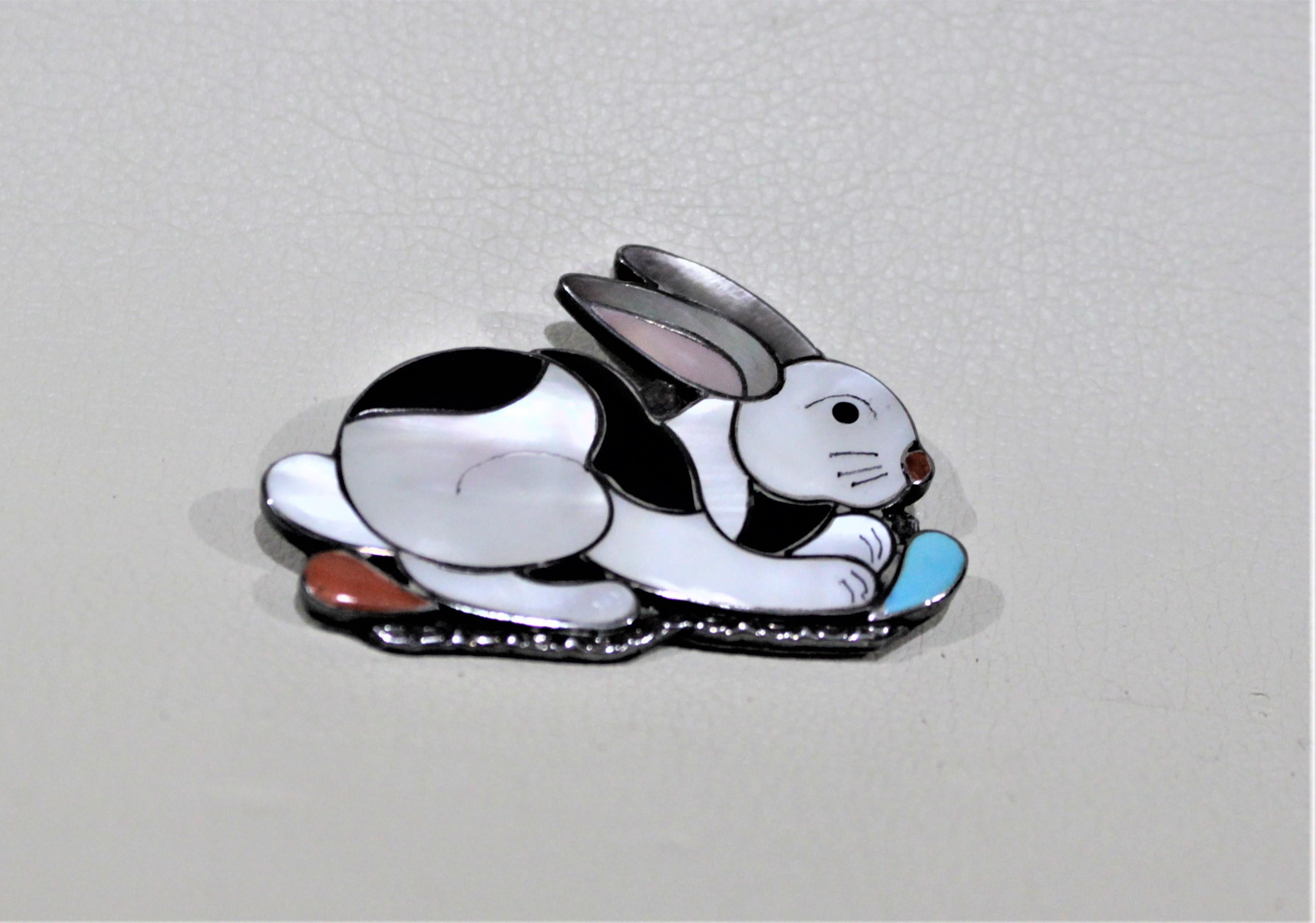 This Zuni Indigenous American sterling silver and inlaid gemstone figural rabbit brooch or pendant was made by Porfillo and Ann Sheyka. The piece was handmade in most likely the late 1960s in the Mid-Century Modern style and is done with a sterling