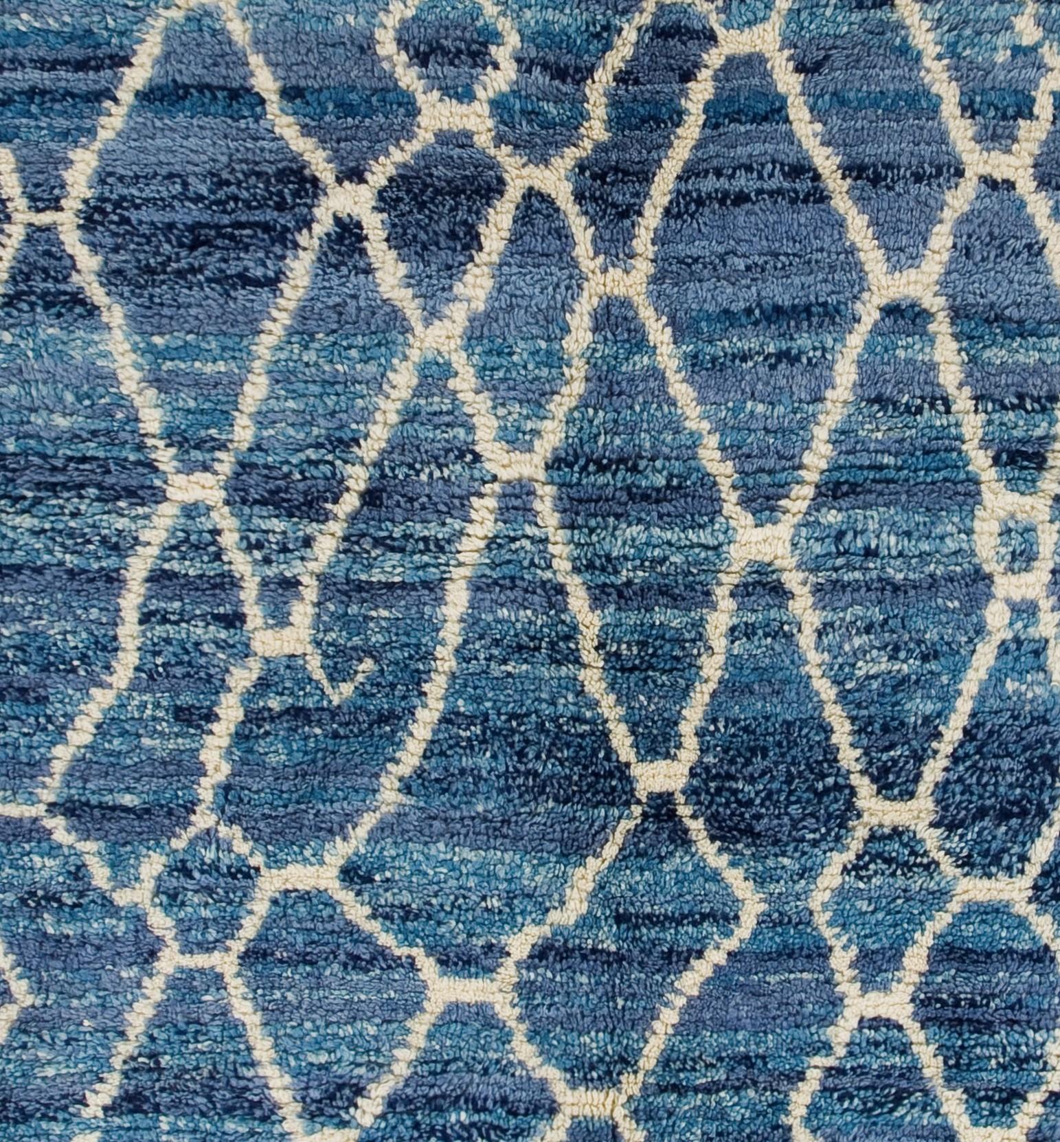 A contemporary, hand-knotted brand new Moroccan rug with an all-over design of irregular, flowing, lozenge shaped lattices in cream against a blue field. The slightly darker and lighter hues of the striated blue  of the field creates a shimmering of