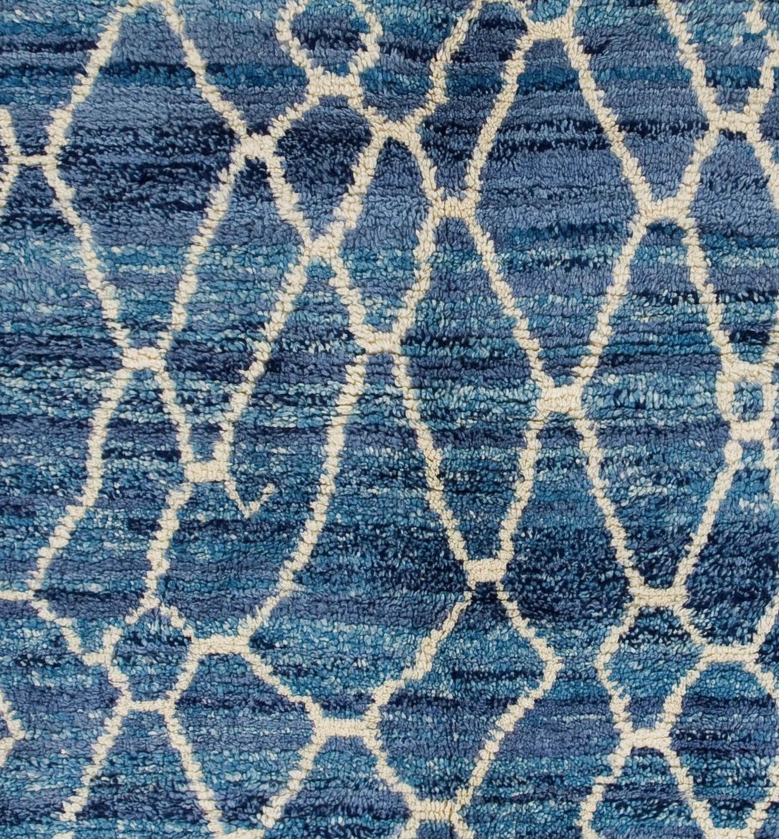 Un tapis marocain contemporain, noué à la main, avec un motif de treillis irréguliers, fluides, en forme de losange, de couleur crème sur un fond bleu. Les teintes légèrement plus foncées et plus claires du bleu strié  du champ crée un effet de
