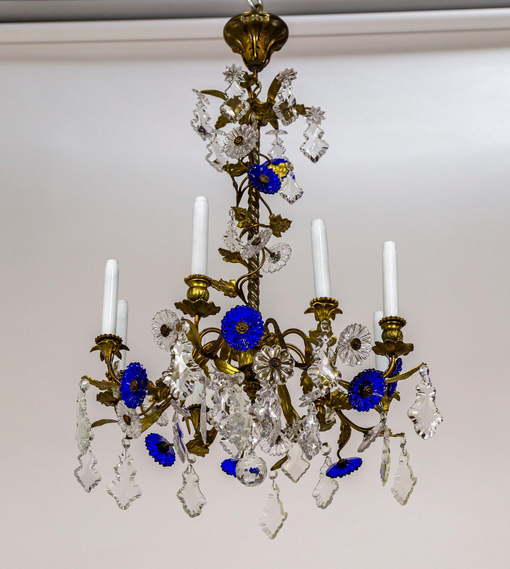 An Art Nouveau, 8-light chandelier with vibrant, deep blue molded crystal flowers and clear crystals in varying shapes. Unique in that arms vary in height for added interest; alternating designs of decorative, floral details on the cast brass candle