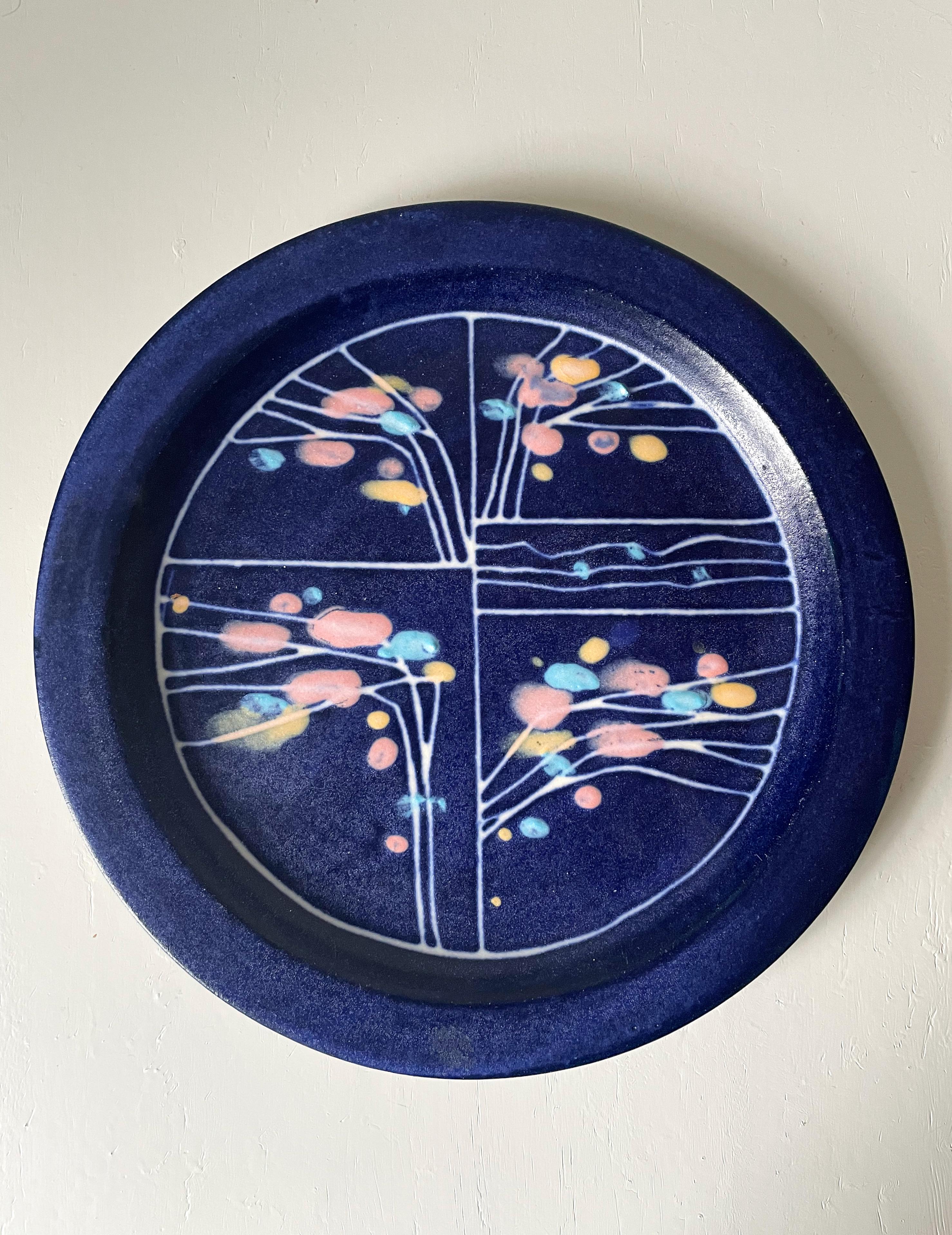 Unique handmade indigo blue ceramic plate for wall or table decoration. Pastel blue, rose and yellow dots placed along white lines resembling floral branches. Signed by artist on back. Beautiful condition. 
Jutland, Denmark, 2010s.