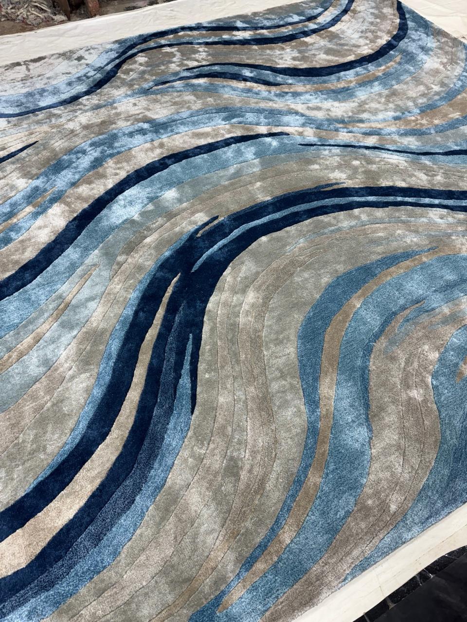 INDIGO est un tapis fluide qui capture le rythme de l'eau en mouvement. Les lignes ondulantes dans les tons bleu océan, gris pierre et beige sable créent un sentiment de profondeur et de mouvement, faisant écho aux vagues, aux courants et à