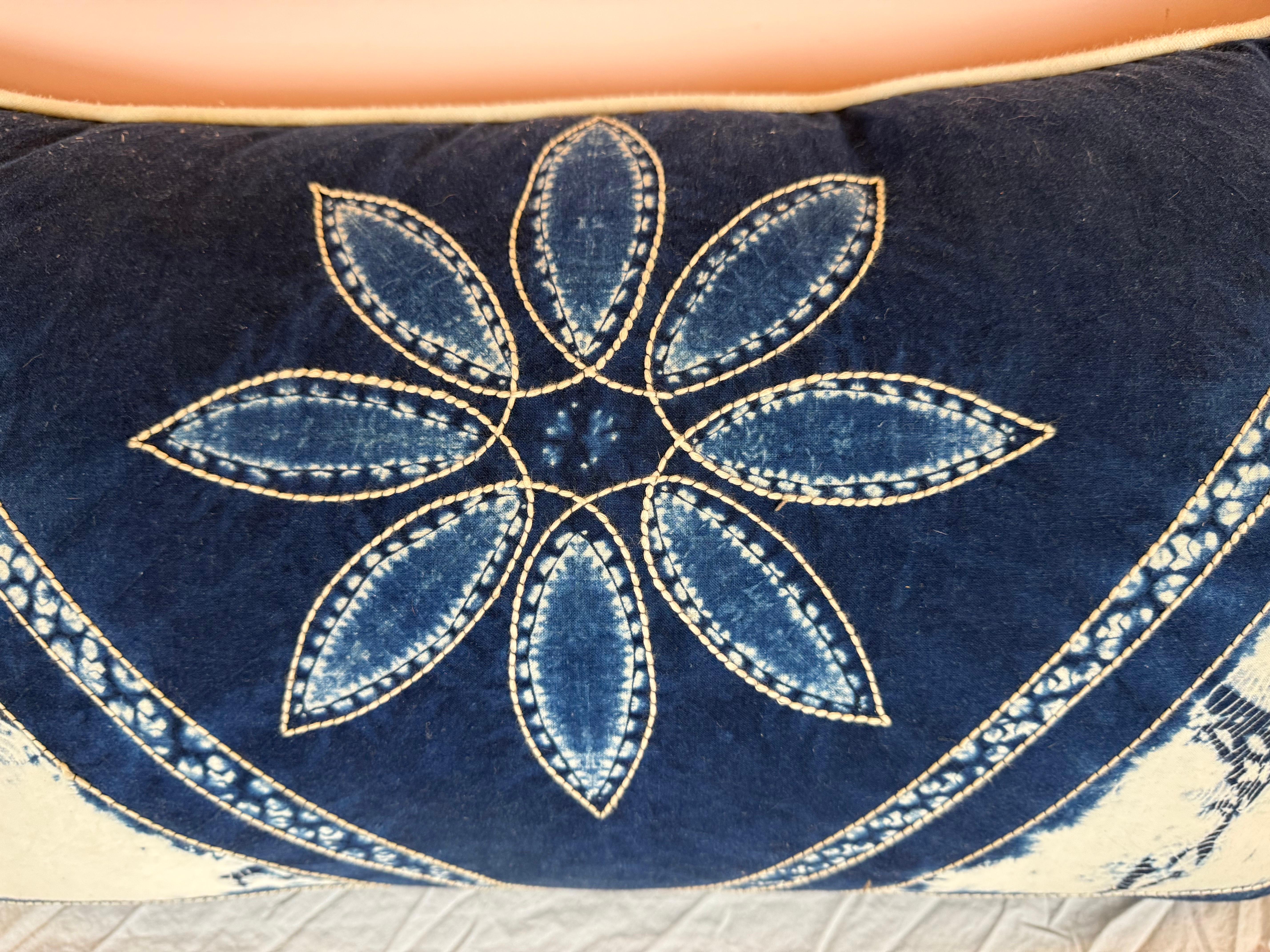 Cet oreiller remarquable présente une face textile teintée à l'indigo, réalisée à la main, avec un motif symétrique audacieux. Au centre se trouve un motif floral stylisé composé de huit pétales ressemblant à des feuilles, chacun étant souligné par