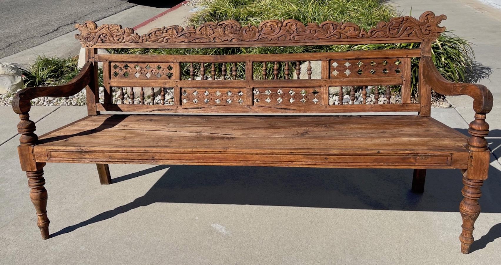 This is a hand-crafted 19th century teak garden bench with intricate carving on the back and carved shaped arms.