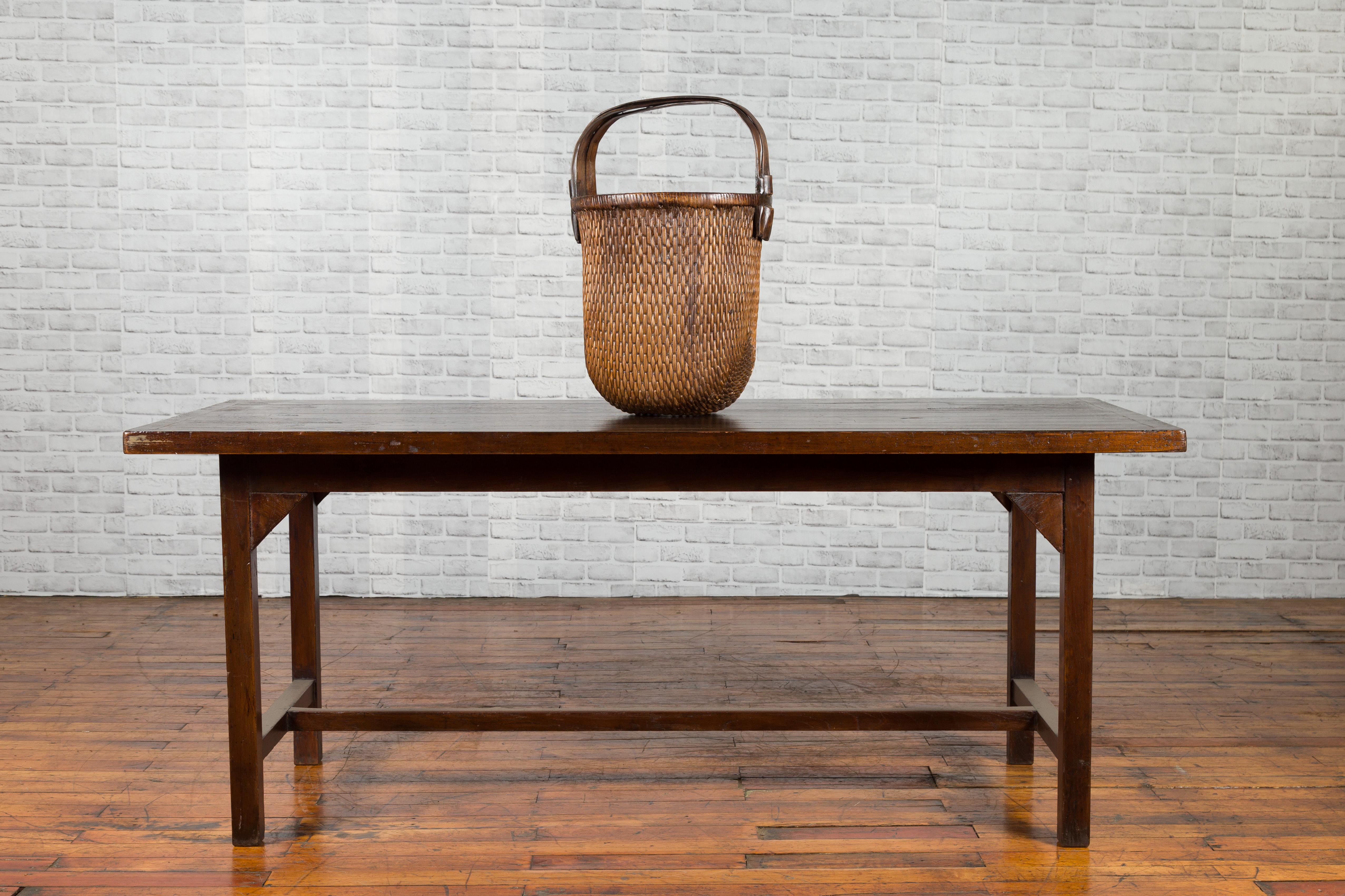 An Indonesian table from the 20th century, with dark patina and H-Form cross stretcher. Created in Indonesia during the 20th century, this dining room table could be also used as a desk. The table features a rectangular planked top sitting above