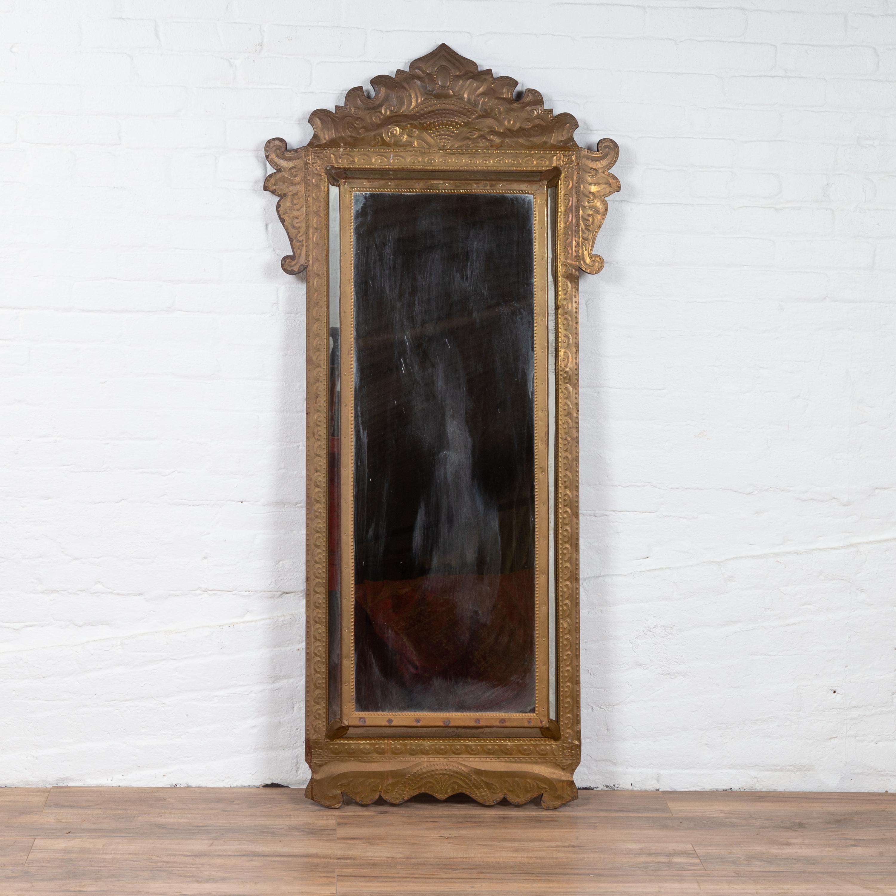 An antique Indonesian brass pareclose mirror from the early 20th century, with flamboyant crest. We have more available. Born in Indonesia during the early years of the 20th century, this charming pareclose mirror features a brass frame adorned with