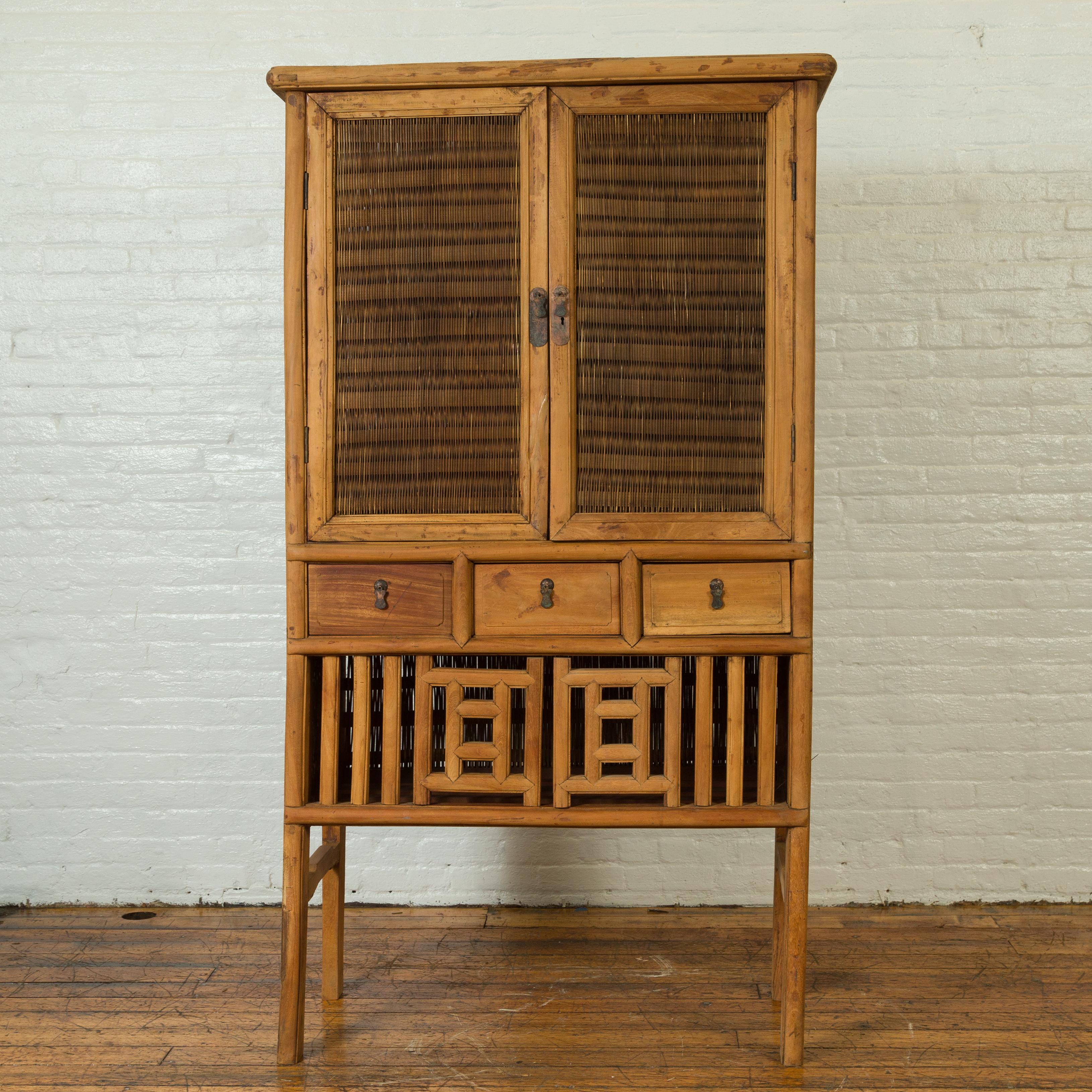 An antique Indonesian kitchen cabinet from the early 20th century, with fretwork sliding doors, drawers and rattan accents. Born in Indonesia during the early years of the 20th century, this rustic cabinet features clean lines, perfectly accented by