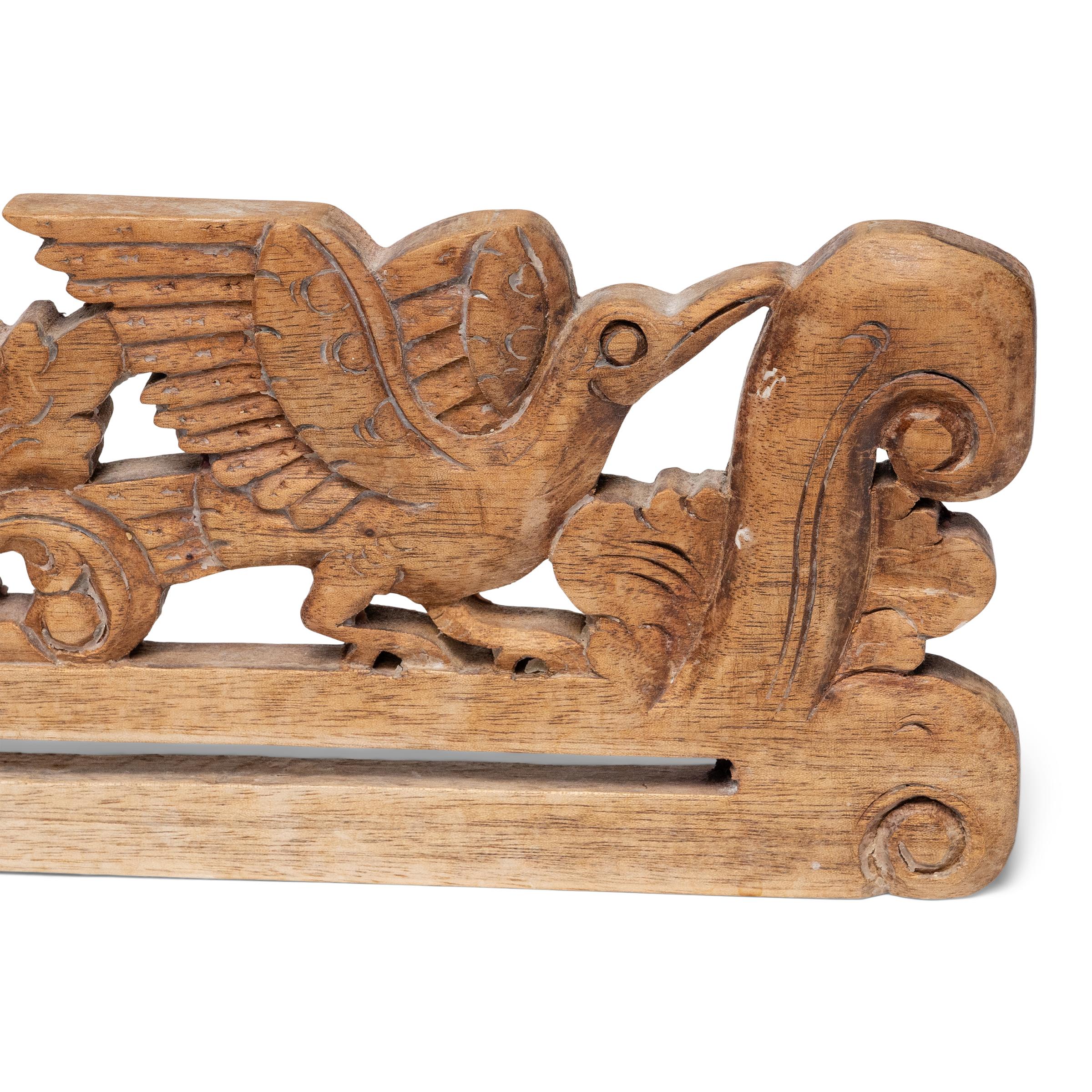 This hand-carved wooden object is an Indonesian wall hanger for displaying batik textiles, woven tapestries or works of embroidery. The hanger is carved with a pierced, low relief design of two birds surrounded by botanical scrollwork. A charming