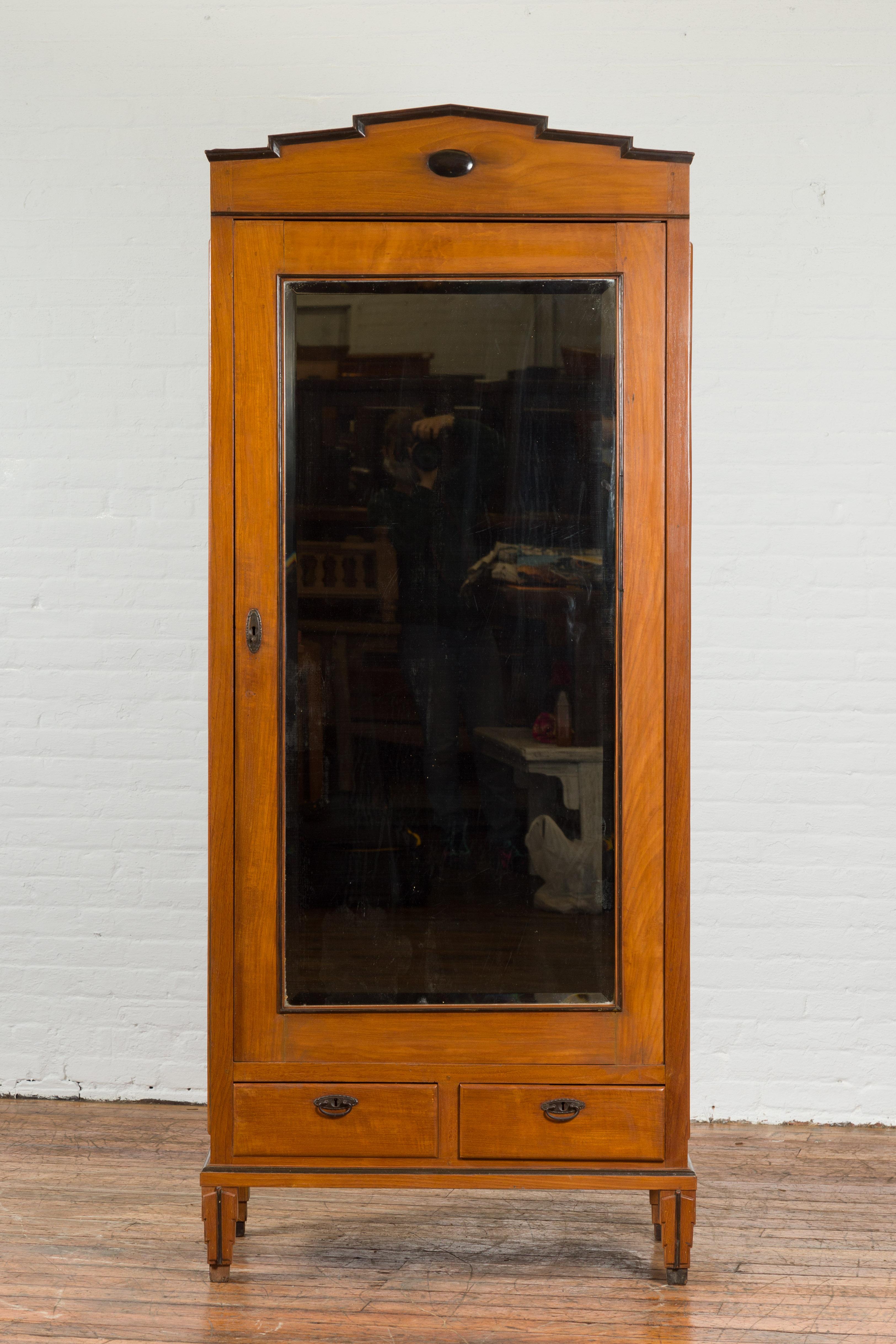 An antique Indonesian cabinet from the early 20th century, with single mirrored door and carved cornice. Created in Indonesia during the early years of the 20th century, this wooden cabinet captures our attention with its stepped cornice with dark
