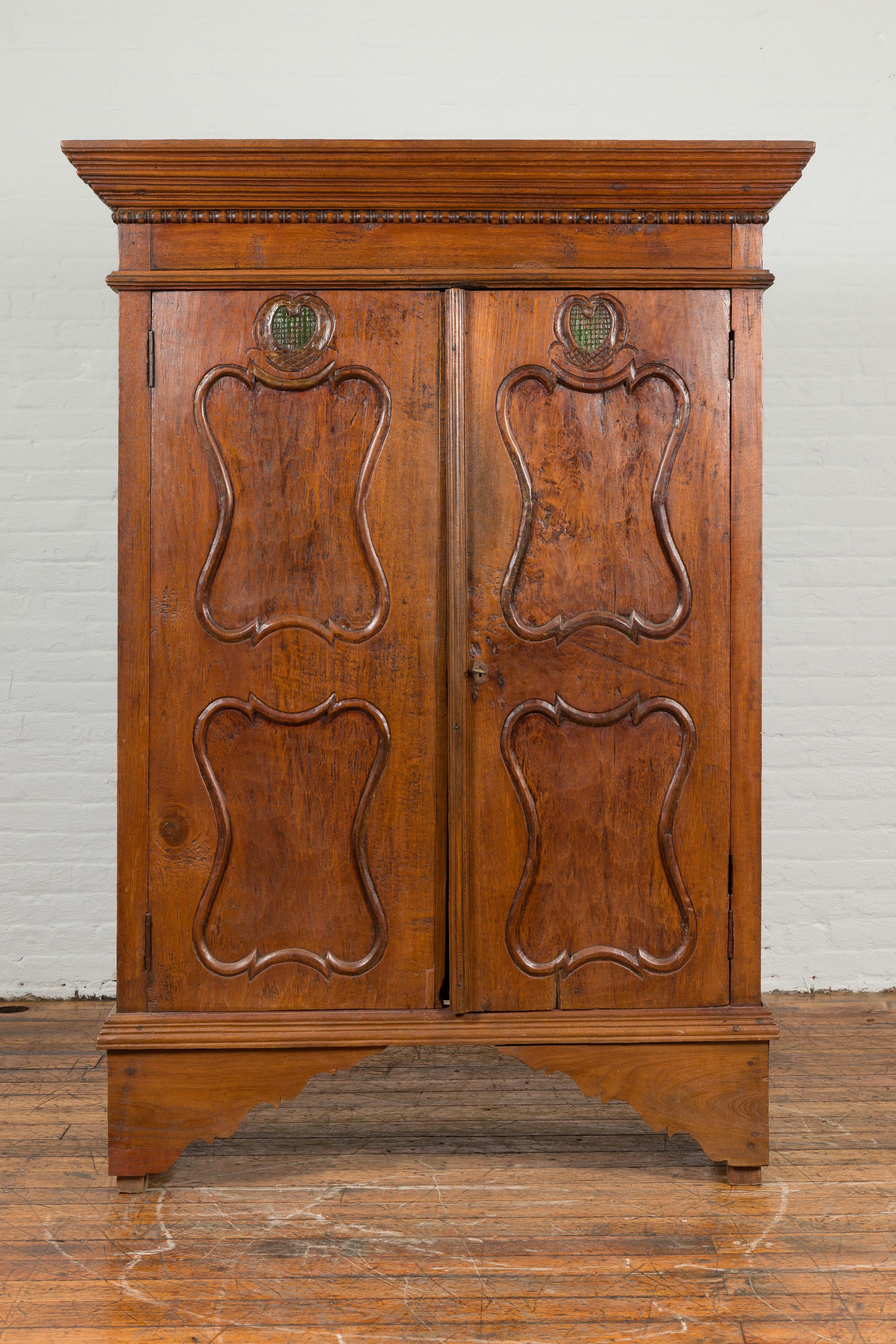 An Indonesian teak wood cabinet from the early 20th century, with carved panels and bracket feet. Created in Indonesia during the early years of the 20th century, this teak wood cabinet features a beveled cornice sitting above a spool style molding.