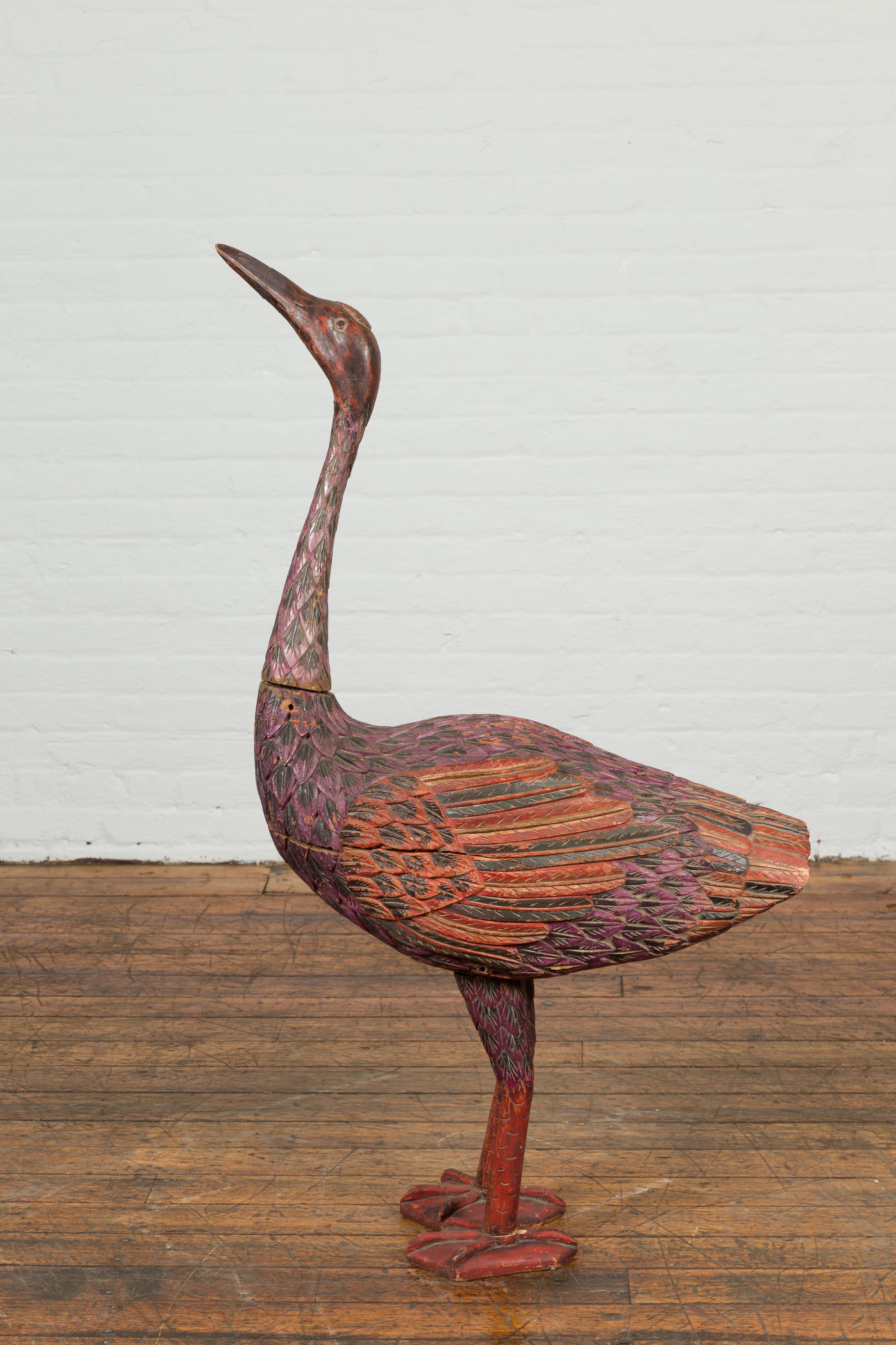 A vintage Indonesian hand carved heron sculpture from the mid-20th century, with polychrome finish. Hand carved in Indonesia during the midcentury period, this sculpture depicts a standing heron looking upwards. Boasting a nicely weathered