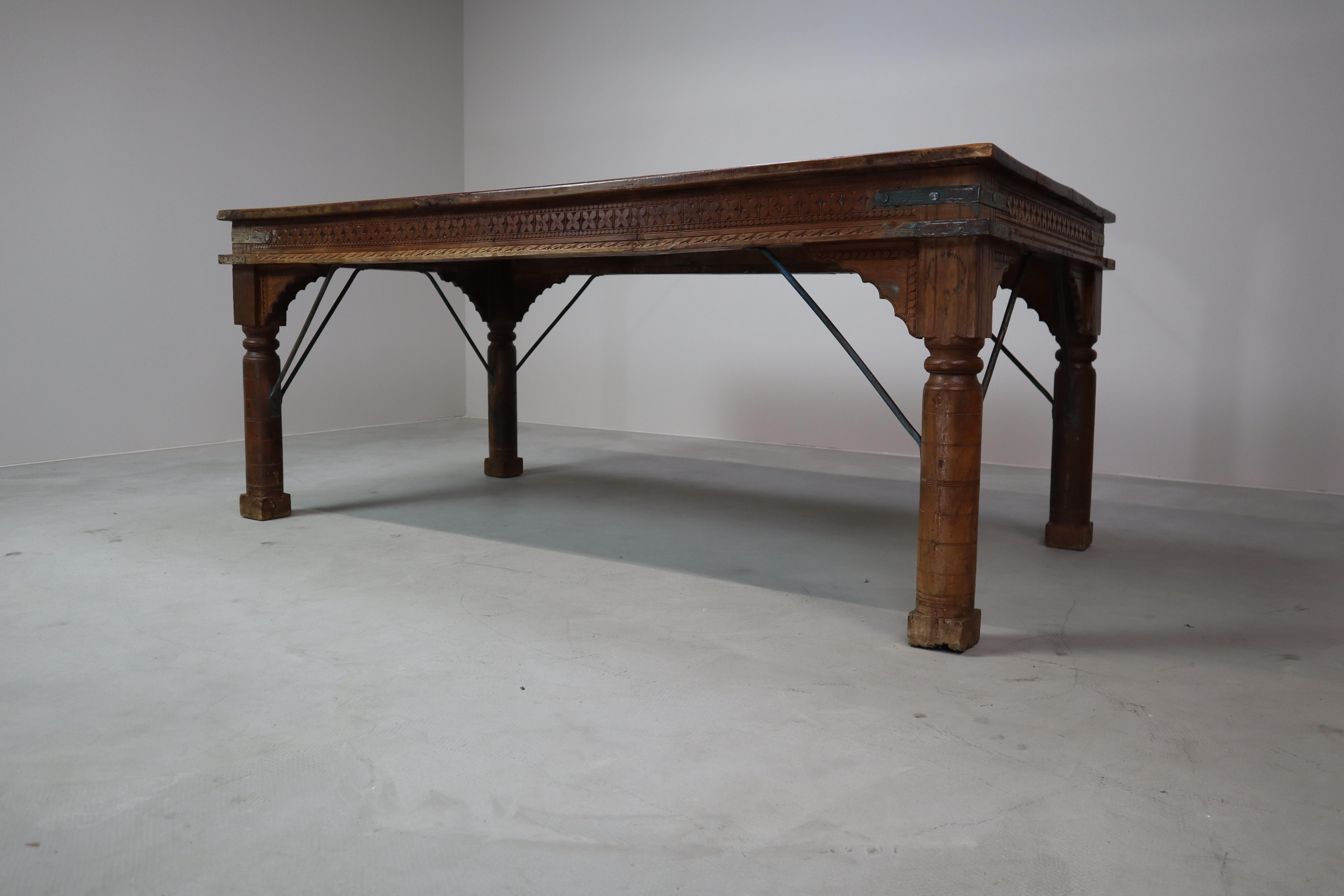 Table de salle à manger unique fabriquée à la main en bois de teck recyclé, originaire d'Indonésie. Cette table allie un savoir-faire authentique à un aspect antique intemporel. Les sculptures détaillées le long des bords et les accents métalliques