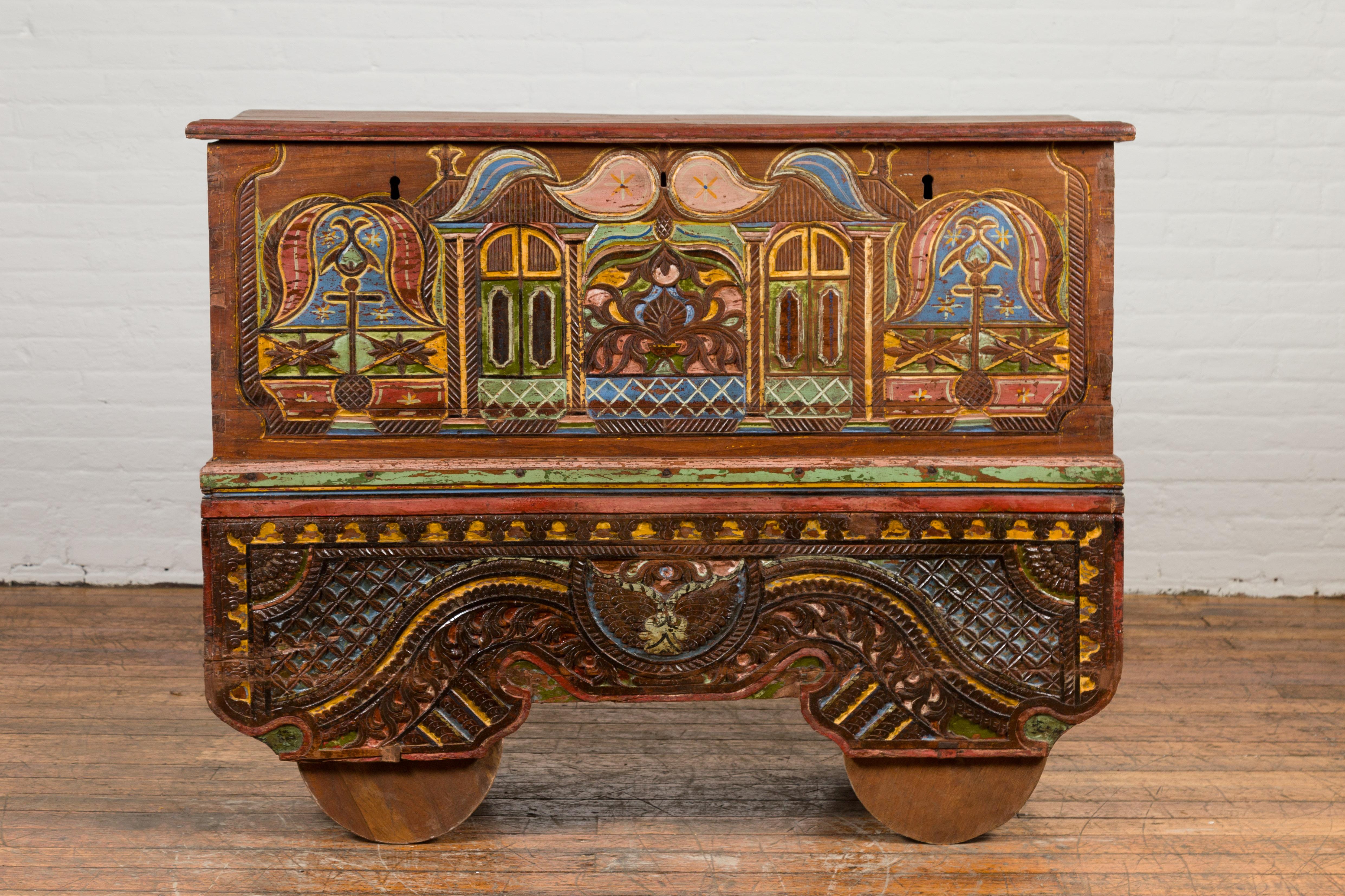 An Indonesian 19th century merchant's blanket chest on wheels from Madura, with hand-painted and carved front showcasing tribal designs. Created in Madura off of the northeastern coast of Java during the 19th century, this merchant's chest draws our