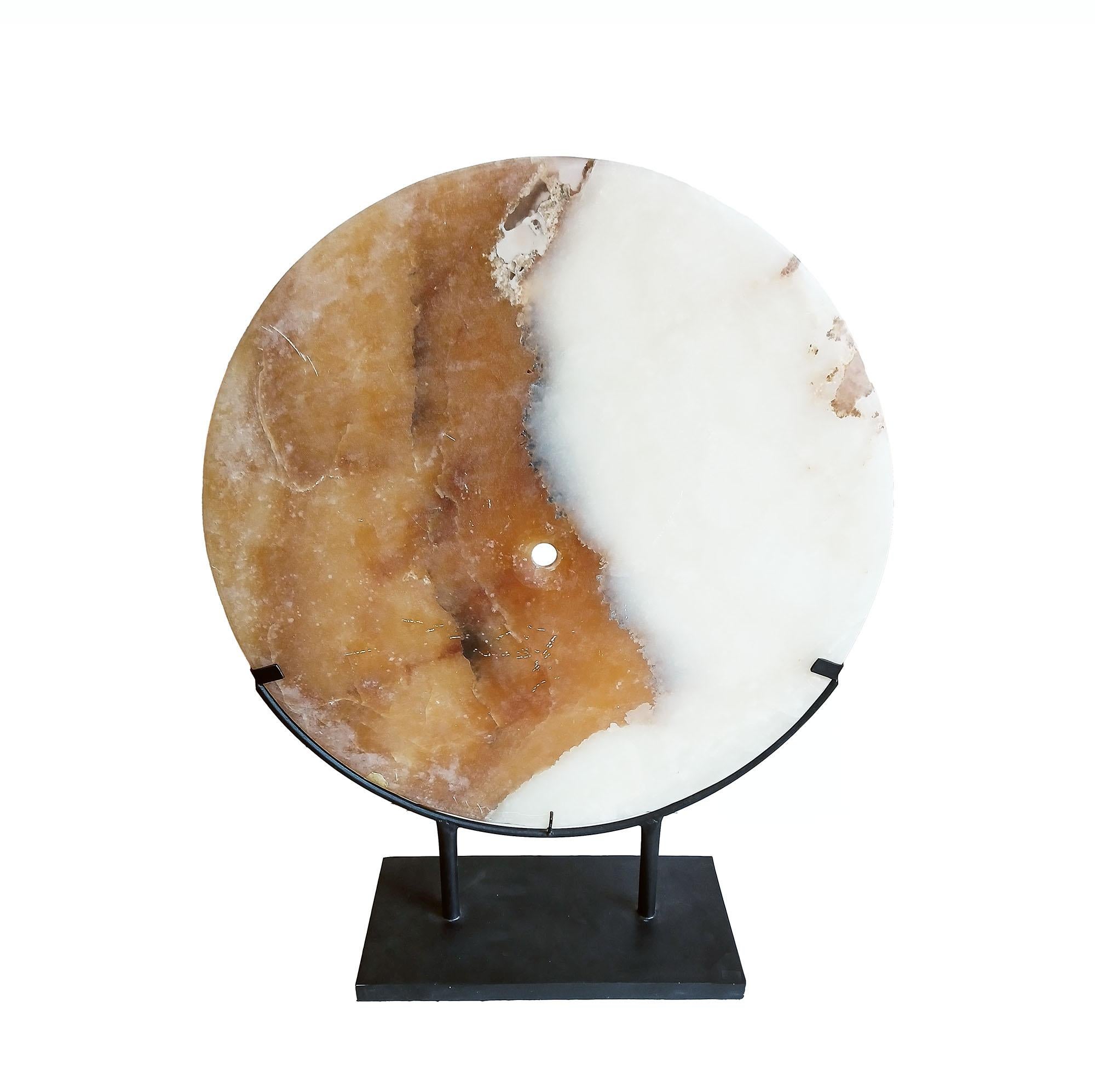 Un sottile disco in pietra d'onice, scolpito a mano in Indonesia, contemporaneo. 
Il disco bicolore proviene da un taglio trasversale di una roccia più grande, che mostra le bande irregolari tra i colori. Questo rende la pietra diversa dall'onice