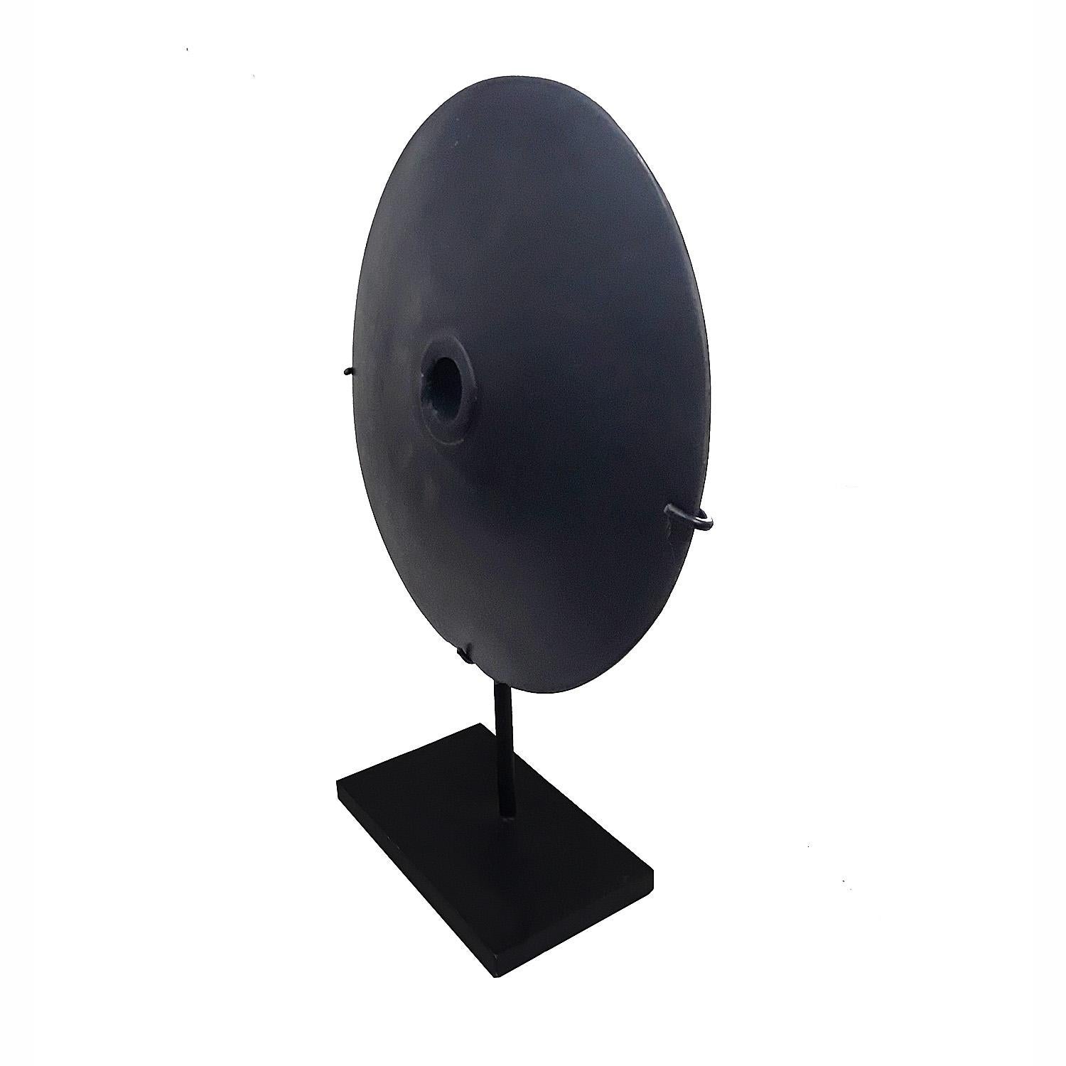 A black stone coin from Indonesia, mounted on a black metal stand. 
14 inches in diameter, 20 inches high. Stand dimensions: 4.5