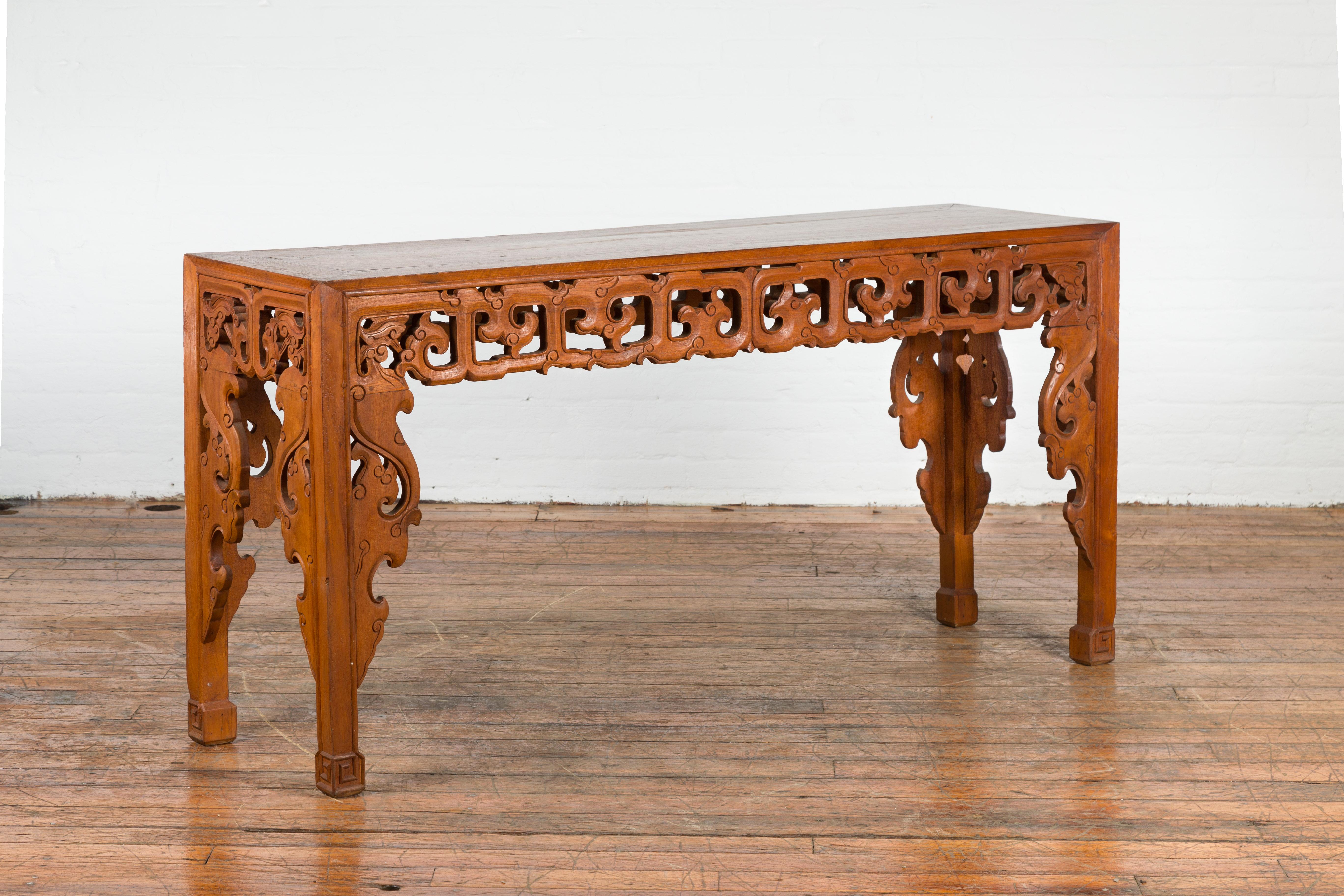 An Indonesian vintage altar console table from the mid 20th century, with carved scrolling clouds. Created in Indonesia during the midcentury period, this altar console table features a rectangular top sitting above a beautifully carved apron