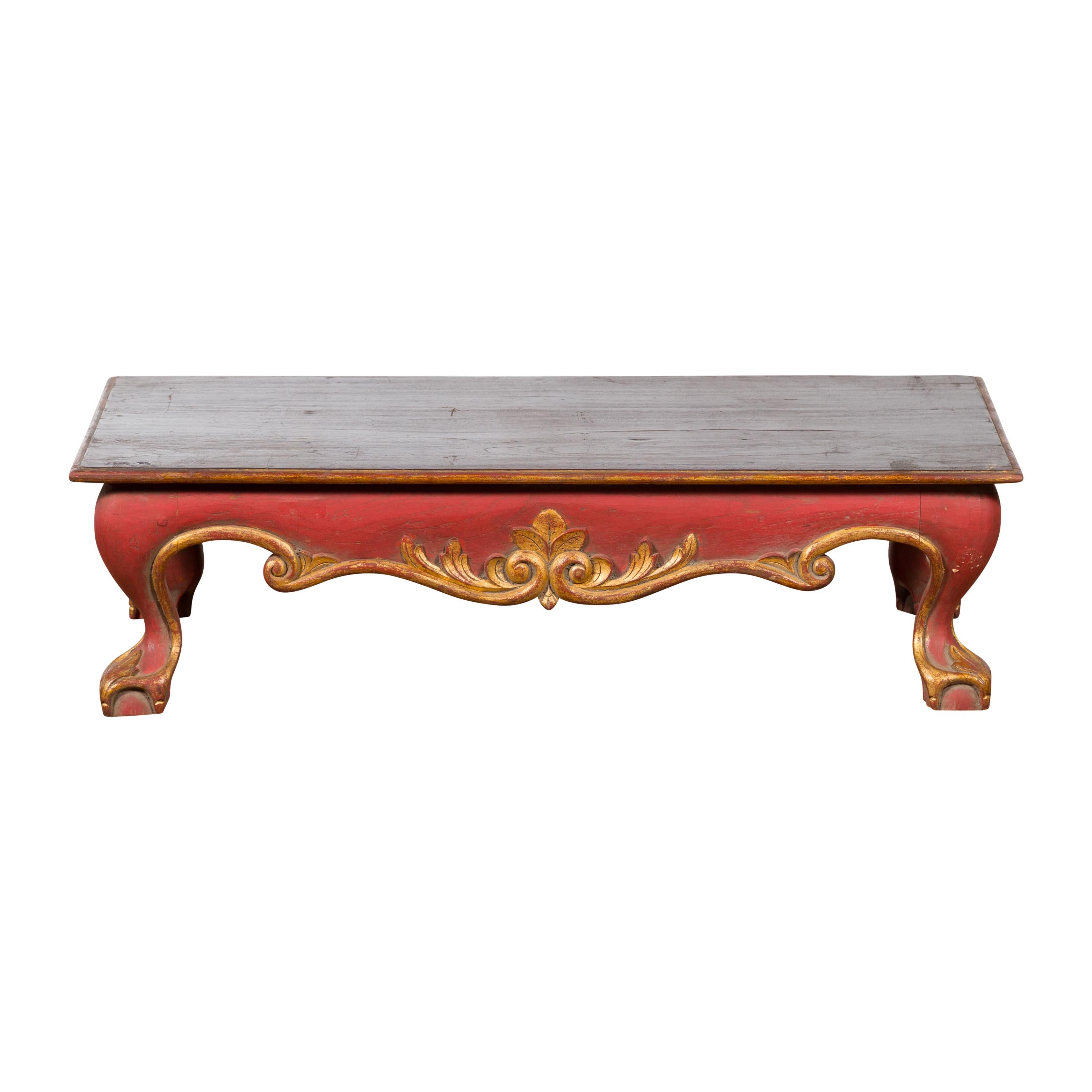 A vintage Indonesian low coffee table from the mid 20th century, with hand-carved apron, gilt accents and ball-and-claw feet. Created in Indonesia during the midcentury period, this coffee table captures our attention with its Rococo style lines as