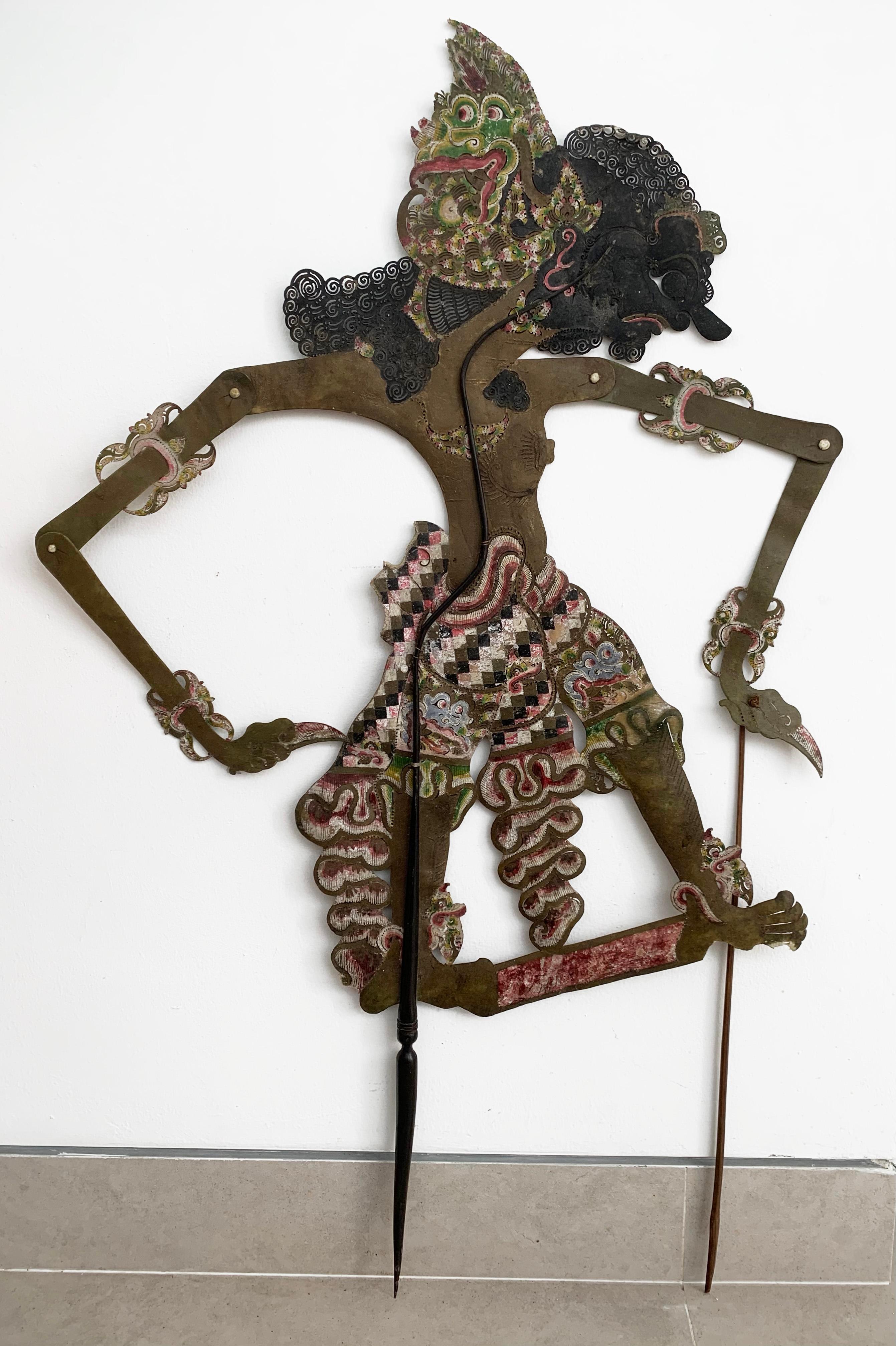 This flat shadow puppet was crafted on the island of Java by a puppet artist using buffalo hide and mounted on bamboo sticks. It features movable arms, controlled by outer bamboo rods (however this puppet lost one of its bamboo rods over the years