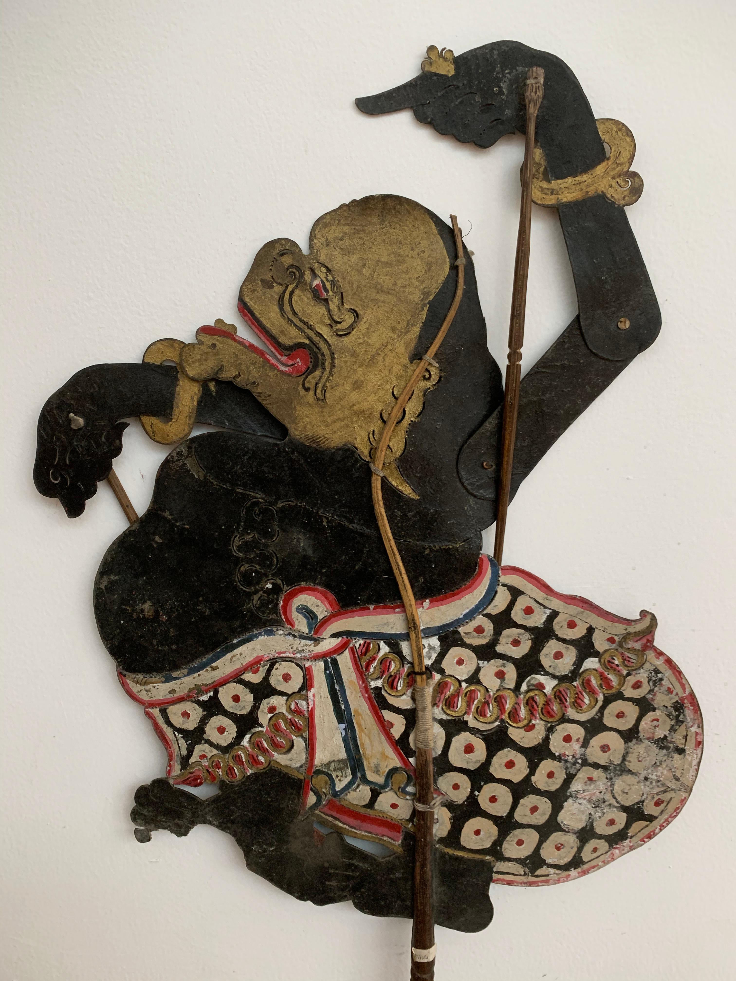 This flat shadow puppet was crafted on the island of Java by a puppet artist using buffalo hide and mounted on bamboo sticks. It features movable arms, controlled by outer bamboo rods. It was used in Wayang puppet shows, a type of shadow puppet show
