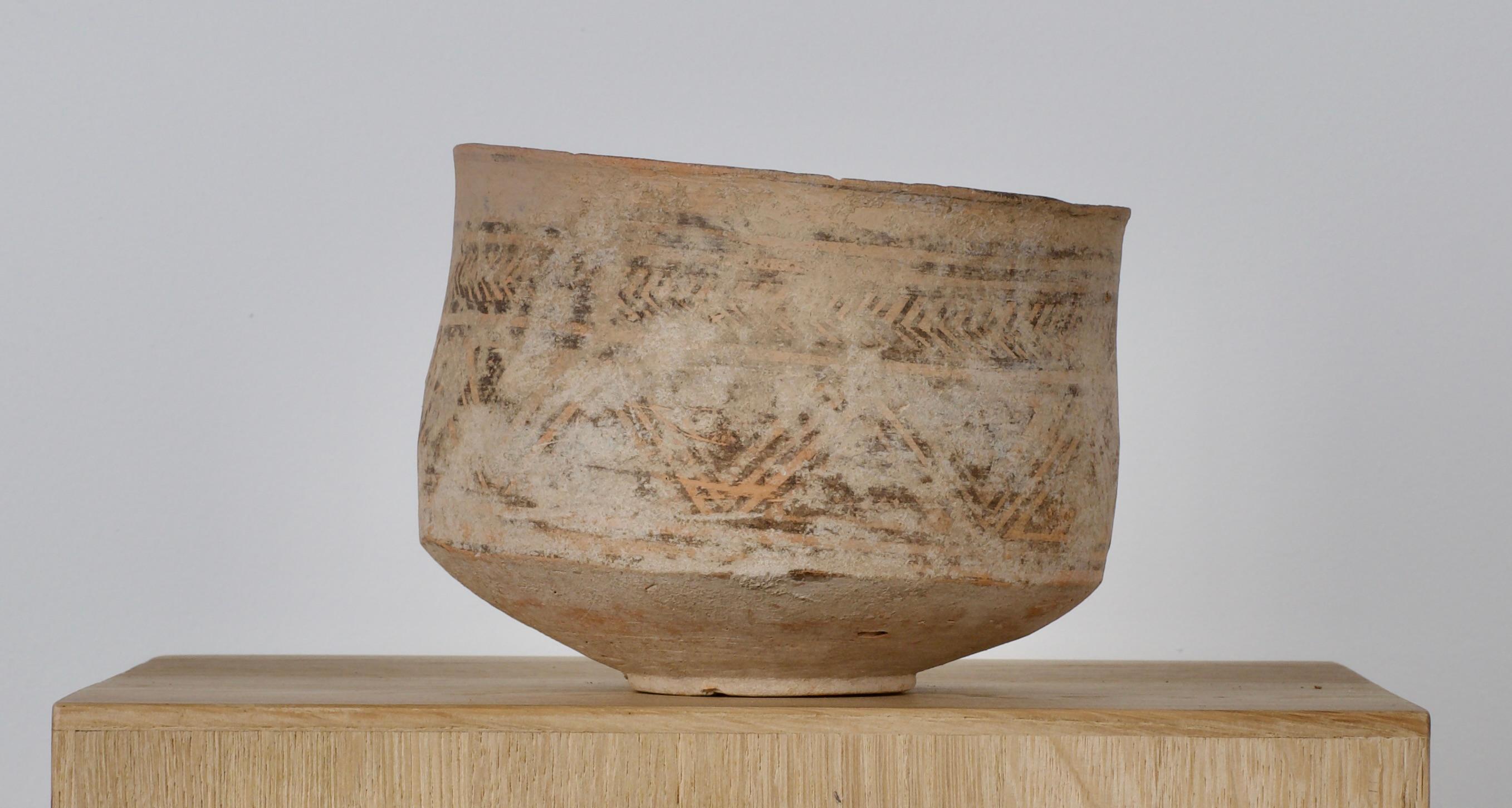 With slightly sloping sidewall and everted rim, narrow foot; painted geometric bands. 
This jar formed from terracotta, exhibits a distinctive form characterized by a flat base, that gracefully tapers towards its pronounced rim. Its structural
