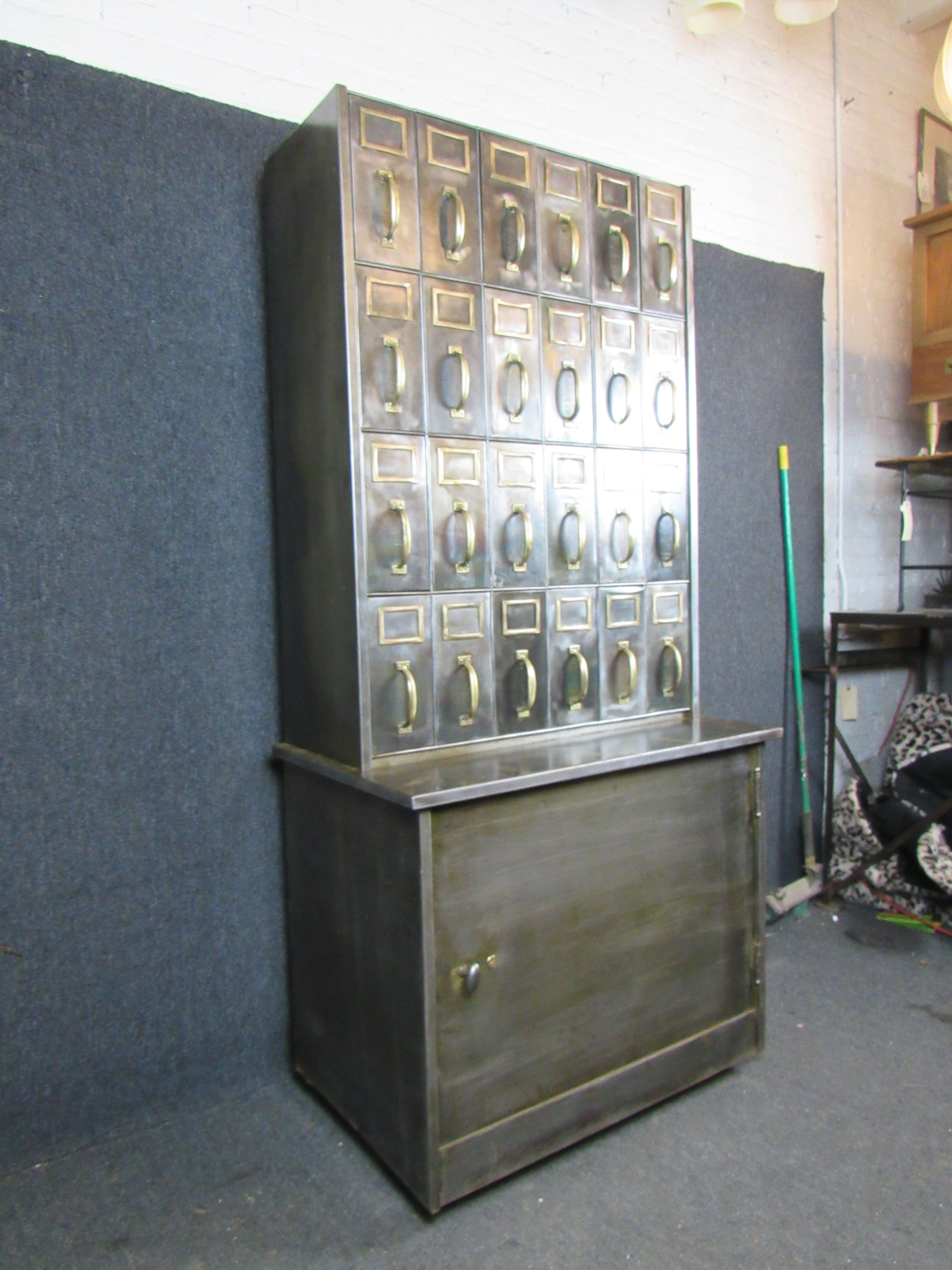 Make a statement in your home or office with this stunning industrial filing cabinet. With an imposing twenty square feet of real steel and aged brass and featuring two dozen pull-out drawers and a large, locking lower cabinet. 
Please confirm item