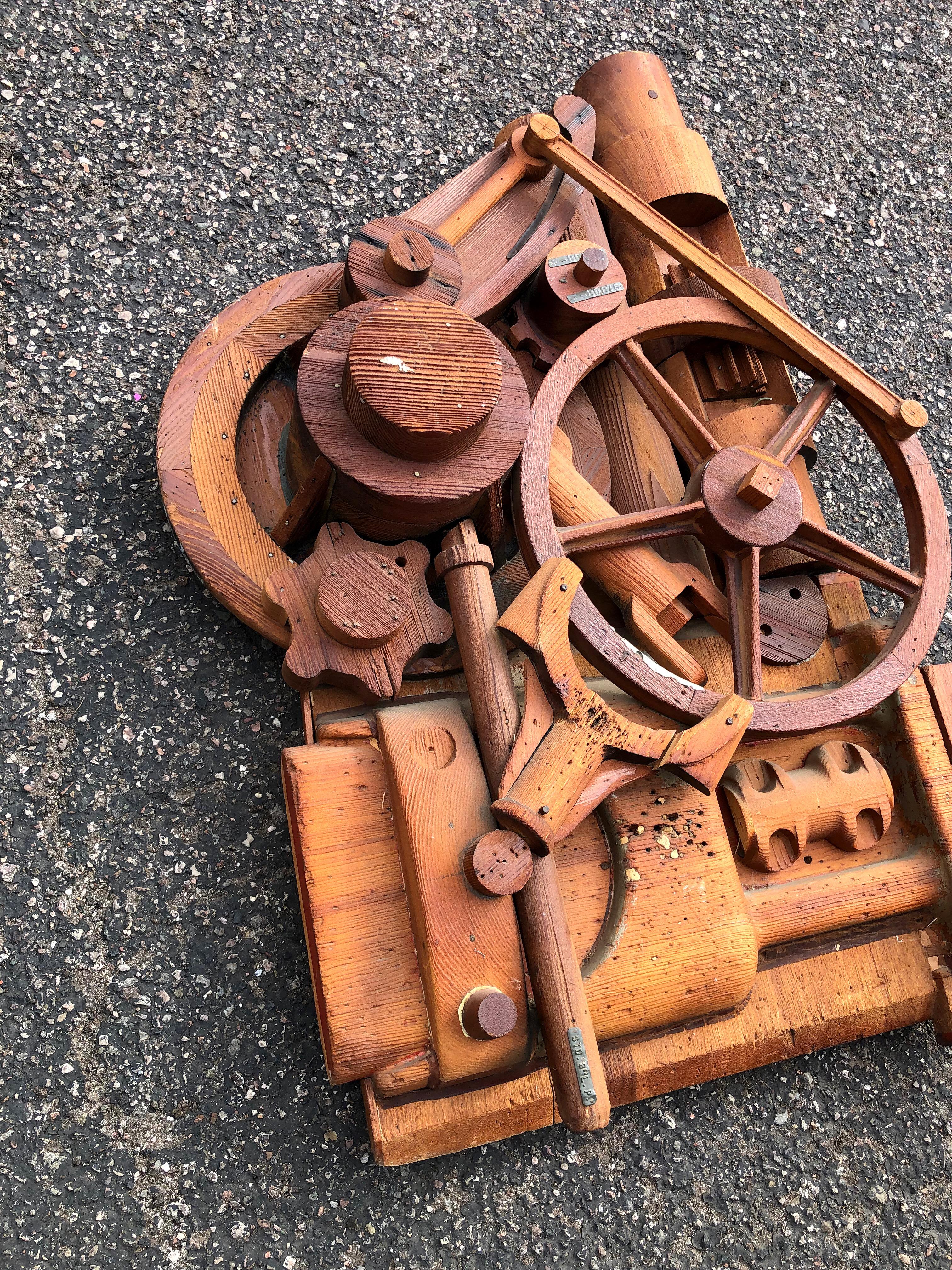 Industrial carved wood sculptural display, with fantastic 3D details. Handcarved with what appears to be reclaimed wood, this piece depicts an assortment of machinery parts, almost like an engine, with cogs, wheels and turnstiles. Rich wood tones in
