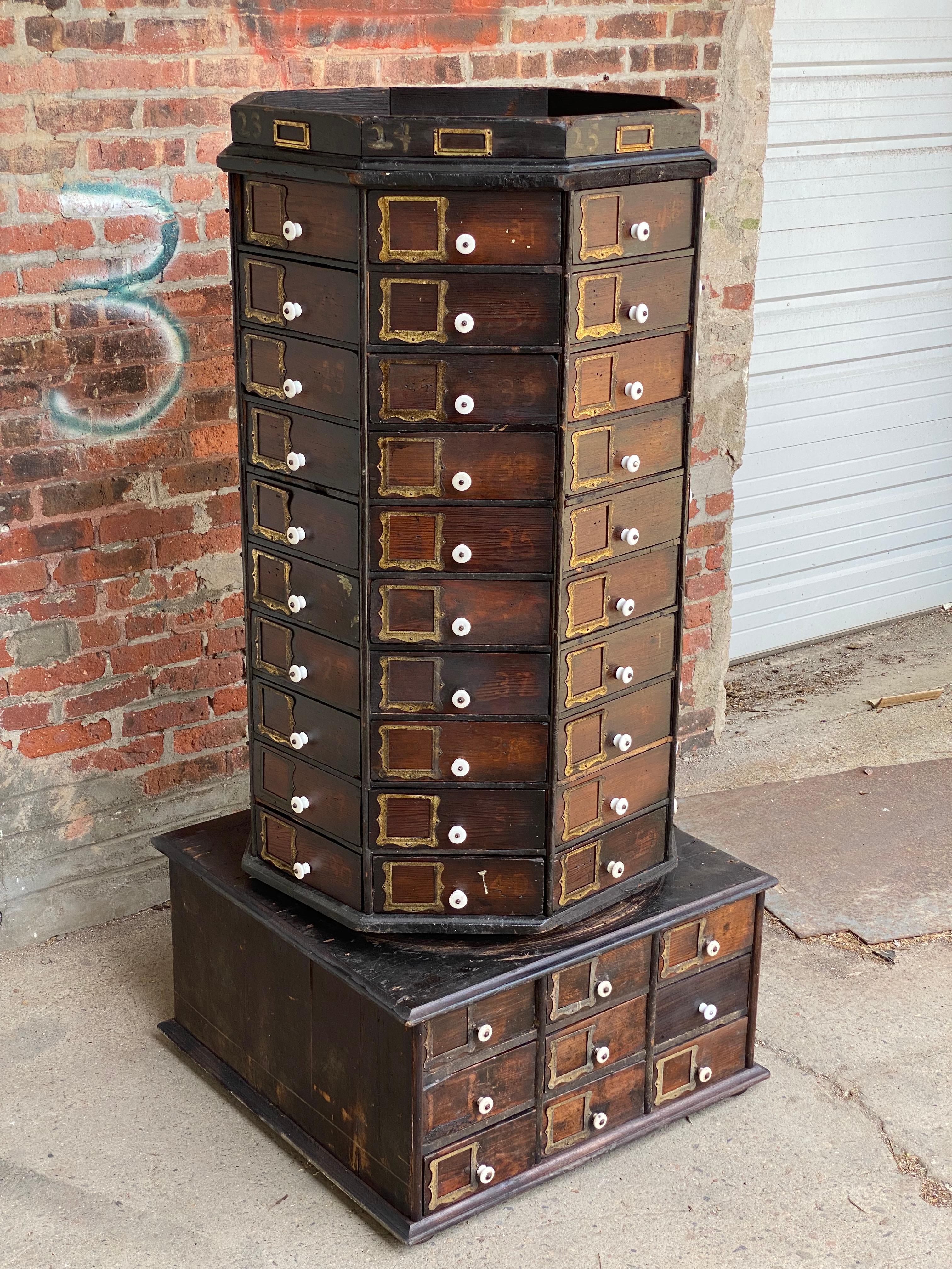 Circa Late Victorian era 98 drawer revolving hardware store cabinet. The spinning octagonal top holds 80 wedge shaped drawers with white porcelain knobs and scalloped edge metal label holders. The base has 18 rectangular shaped drawers, also with