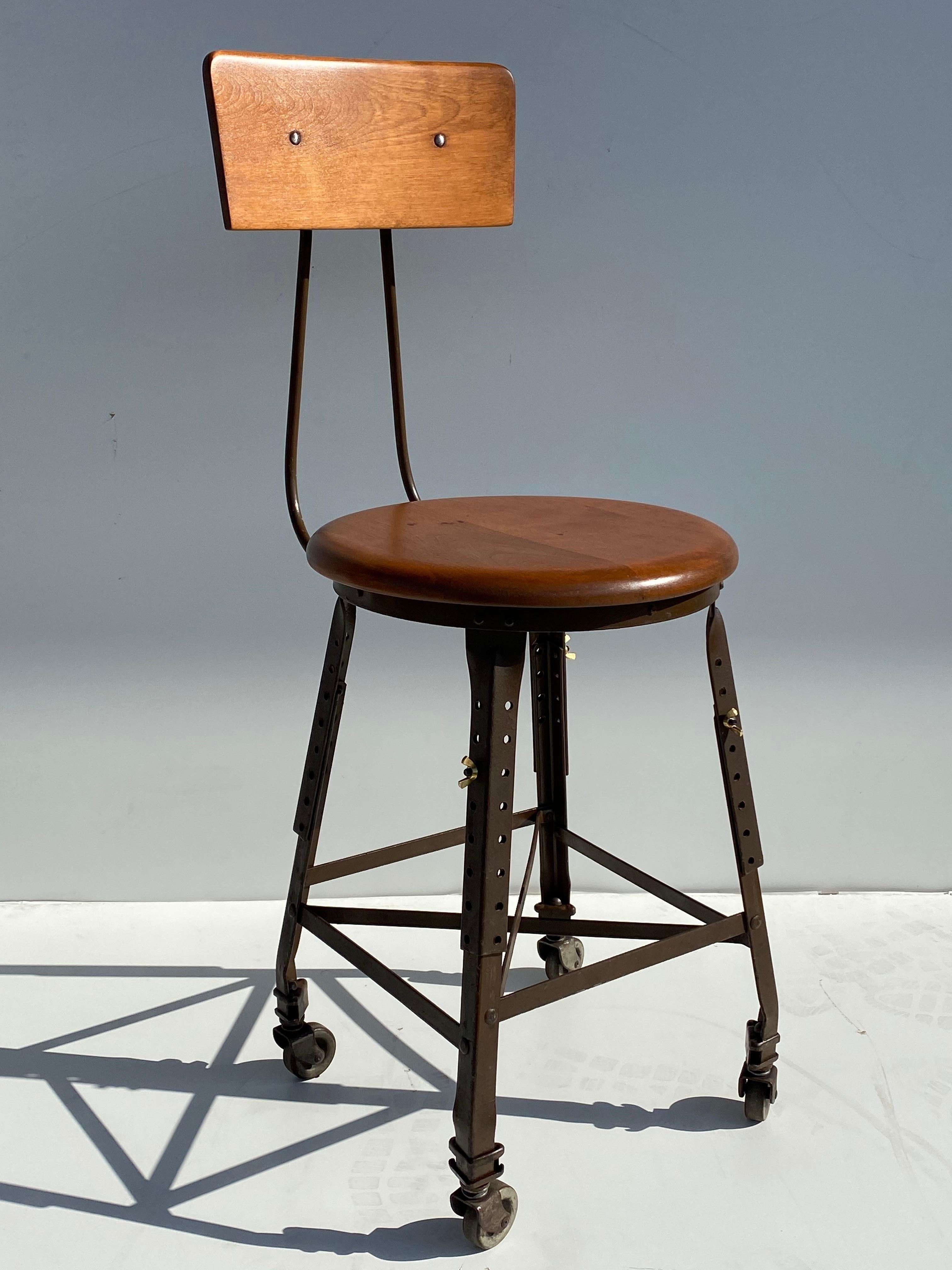 Industrial adjustable artist's stool on casters in maple seat and backrest.