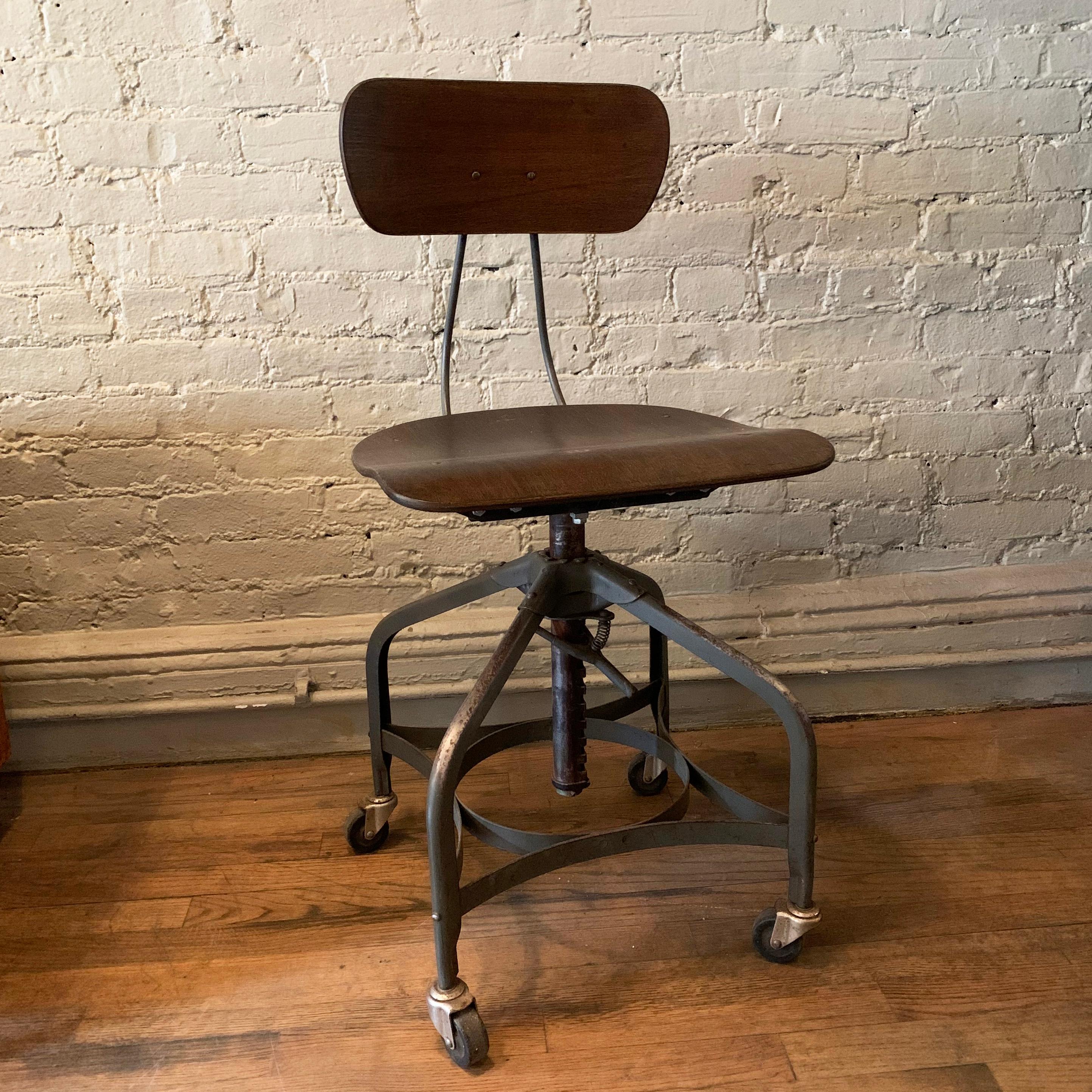 Industrial, rolling, drafting stool by Toledo Metal Furniture Co., features a birch, plywood seat and back with painted steel frame that is seat height adjustable from 19 - 24 inches.