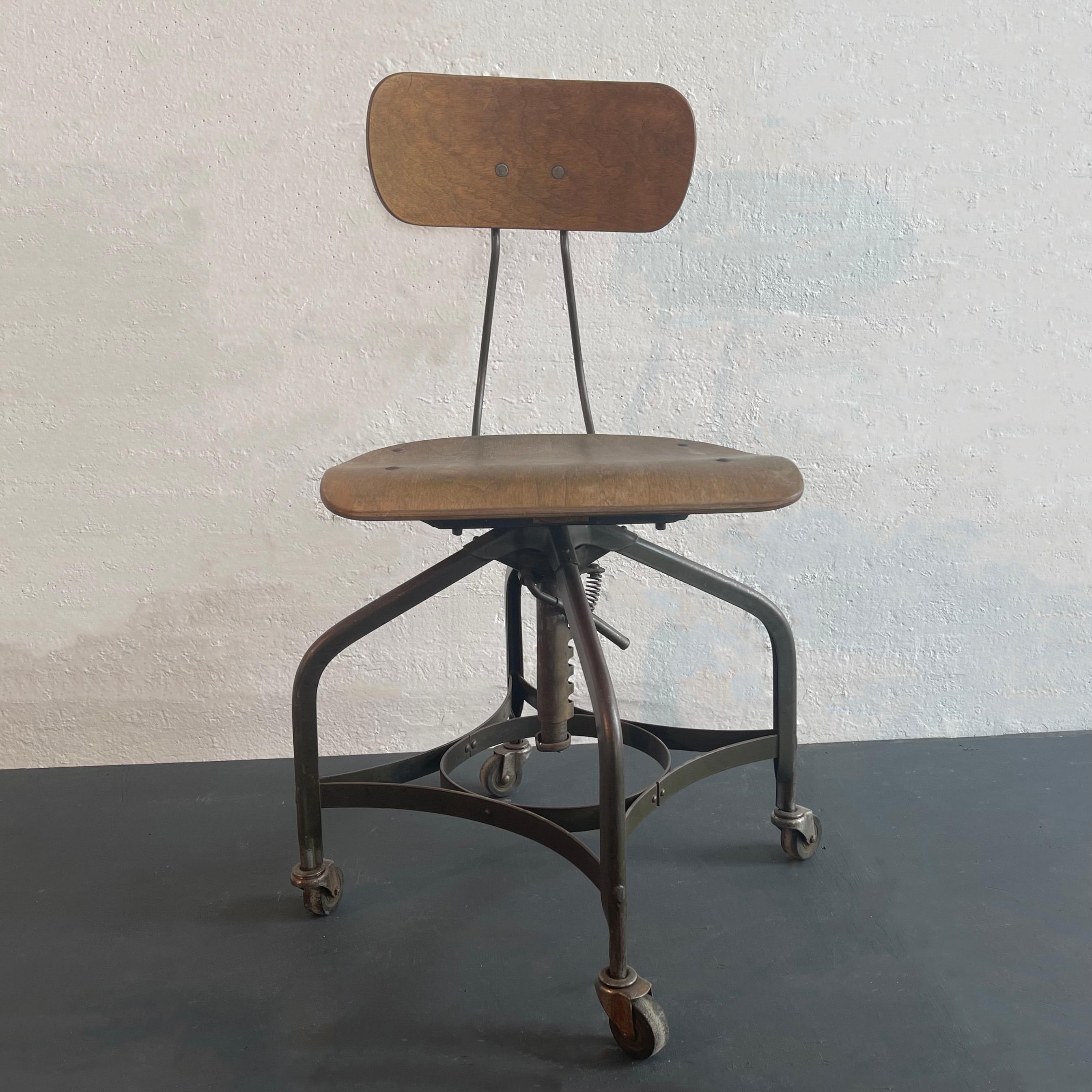 Industrial, swivel, drafting chair by Toledo Metal Furniture Co., circa 1940's features a muted gray green, painted metal frame that rolls on casters with maple seat and back. The chair is height adjustable incrementally from 17 - 21 inches and the