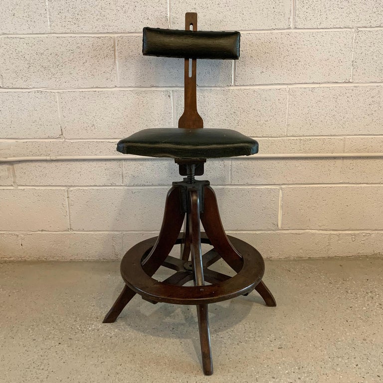Industrial, walnut, telephone operator's swivel stool features the original woven vinyl fabric upholstered seat and back with wide footrest. The 16 W x 14 D seat is height adjustable from 24-27 inches and the backrest is also height adjustable.
