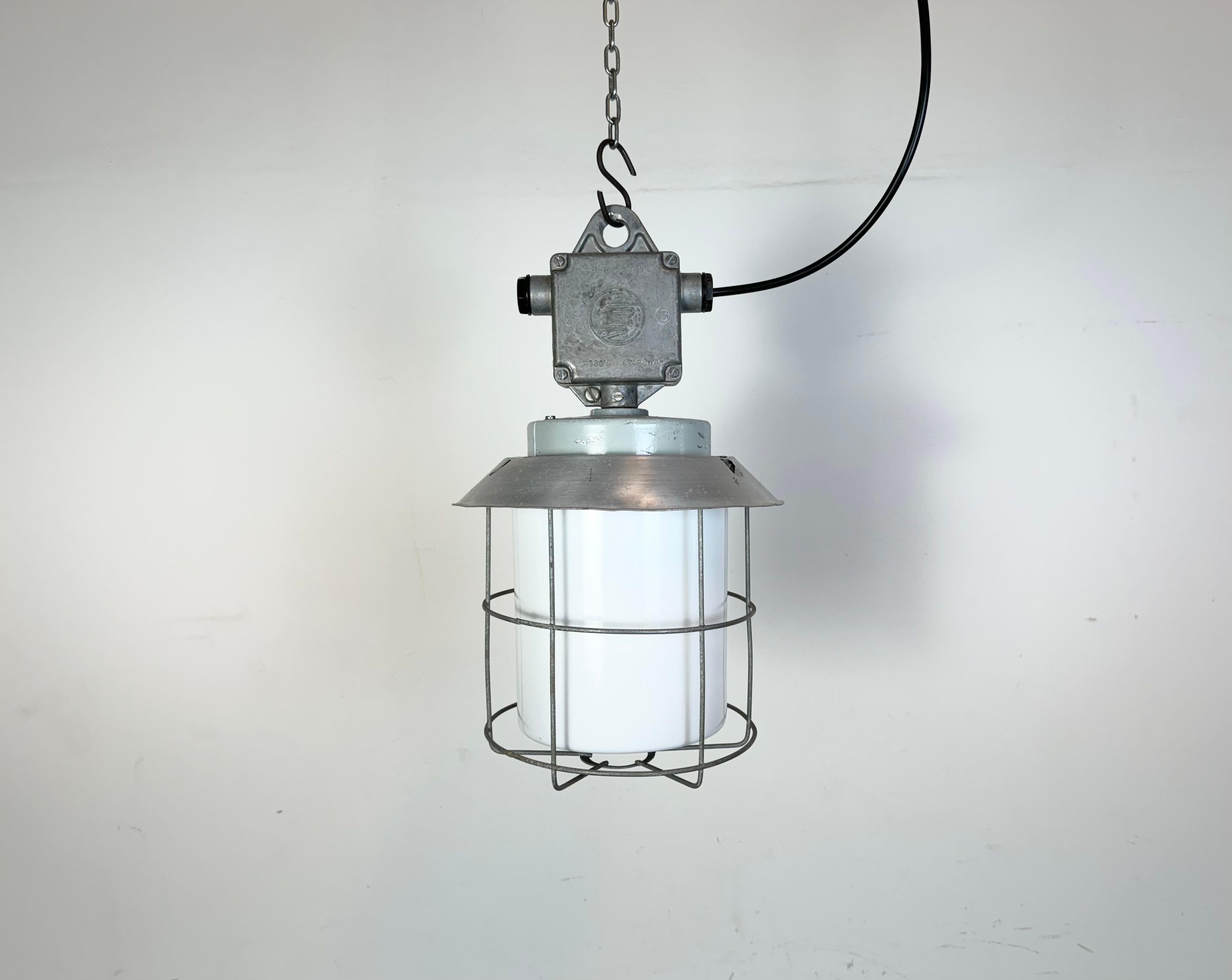 This Industrial hanging light was made by Elektrosvit in former Czechoslovakia during the 1970s. It features a cast aluminium top, an aluminium shade a milk glass and an iron grig. New porcelain socket requires standard E 27/ E26 light bulbs. New
