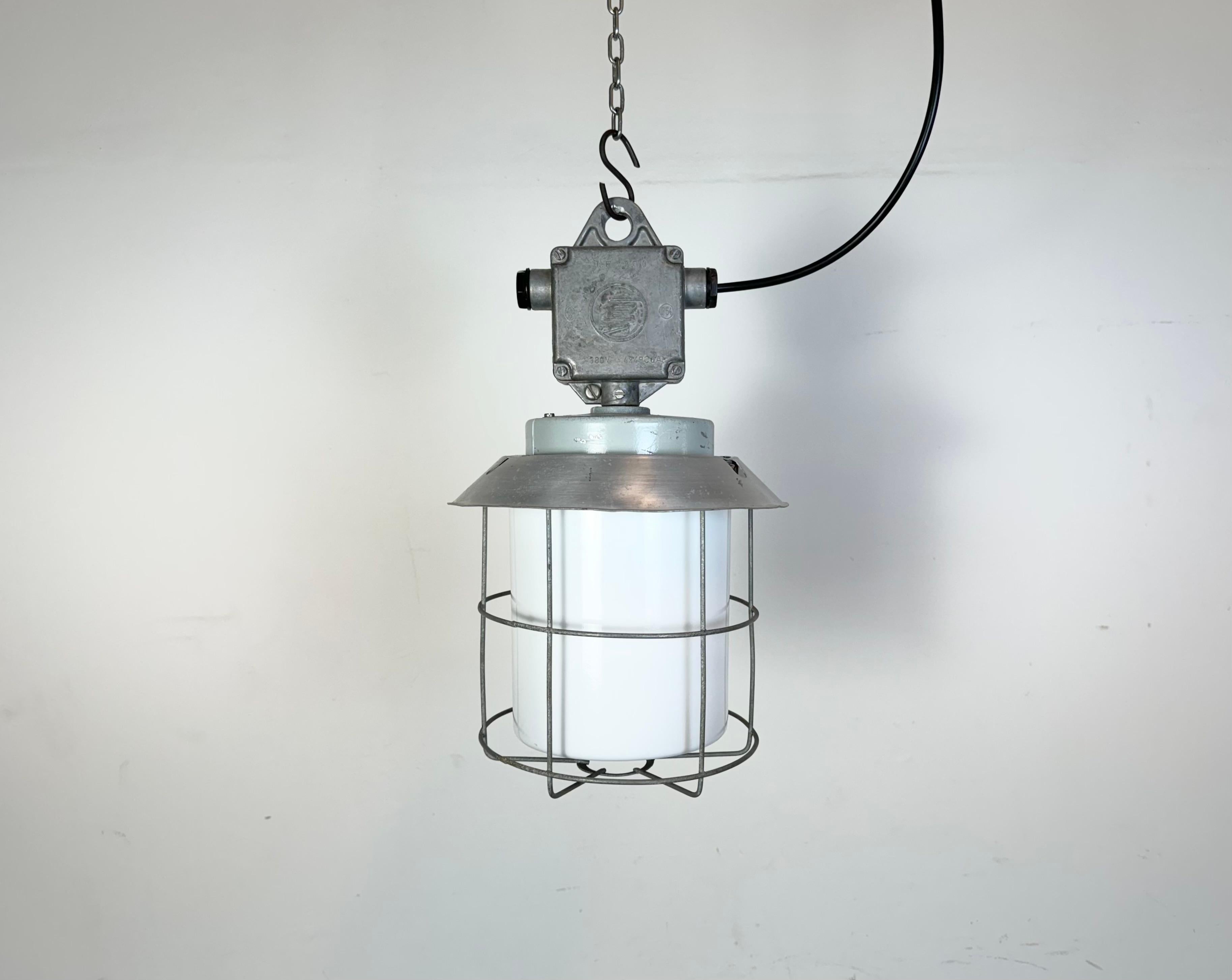 This Industrial hanging light was made by Elektrosvit in former Czechoslovakia during the 1970s. It features a cast aluminium top, an aluminium shade a milk glass and an iron grig. New porcelain socket requires standard E 27/ E26 light bulbs. New