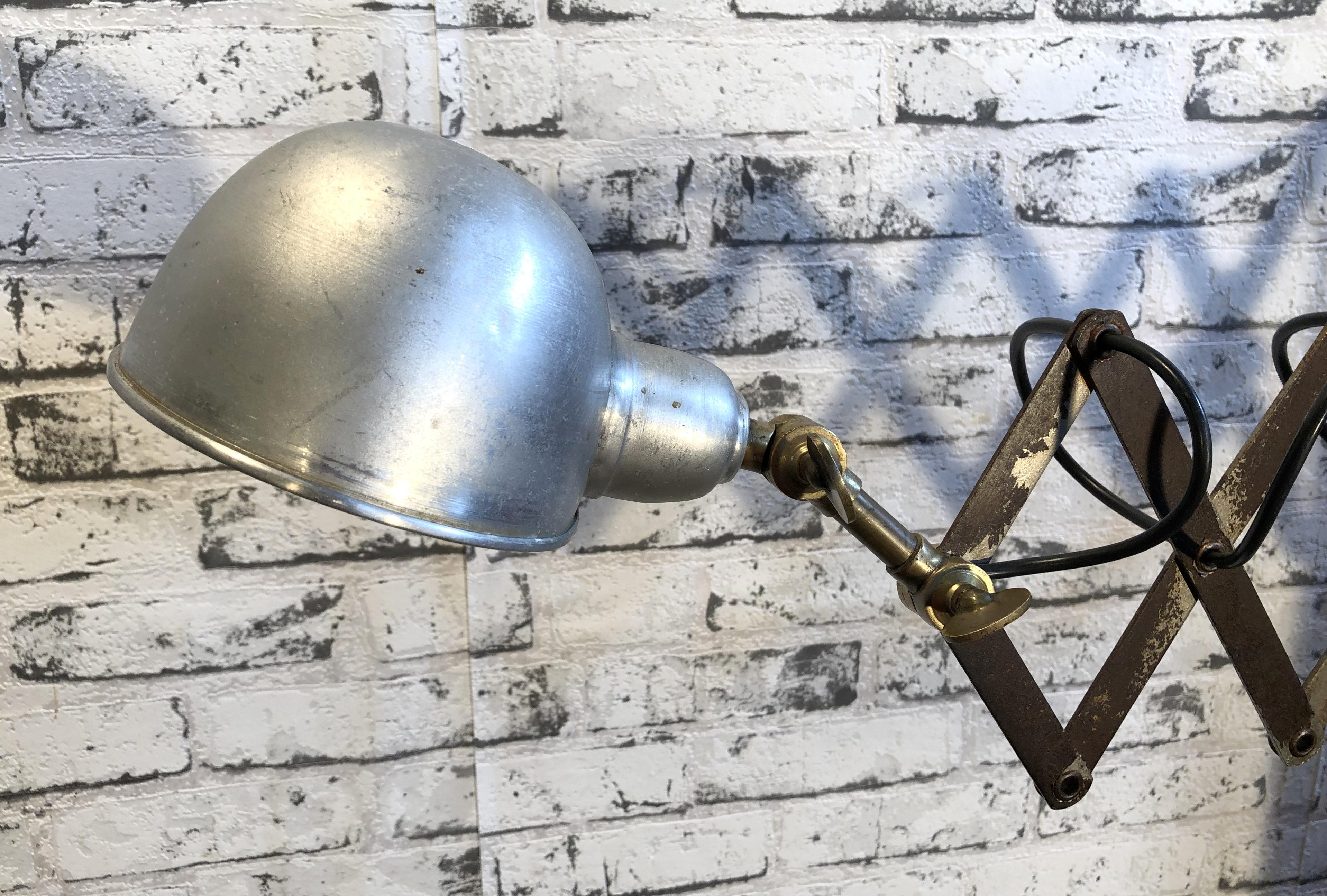 This vintage industrial scissor lamp was produced in former Czechoslovakia during the 1950s. Lamp has silver aluminium shade. Iron scissor arm is extendable and can be turned sideways. Porcelain socket for E 27 lightbulbs. Fully