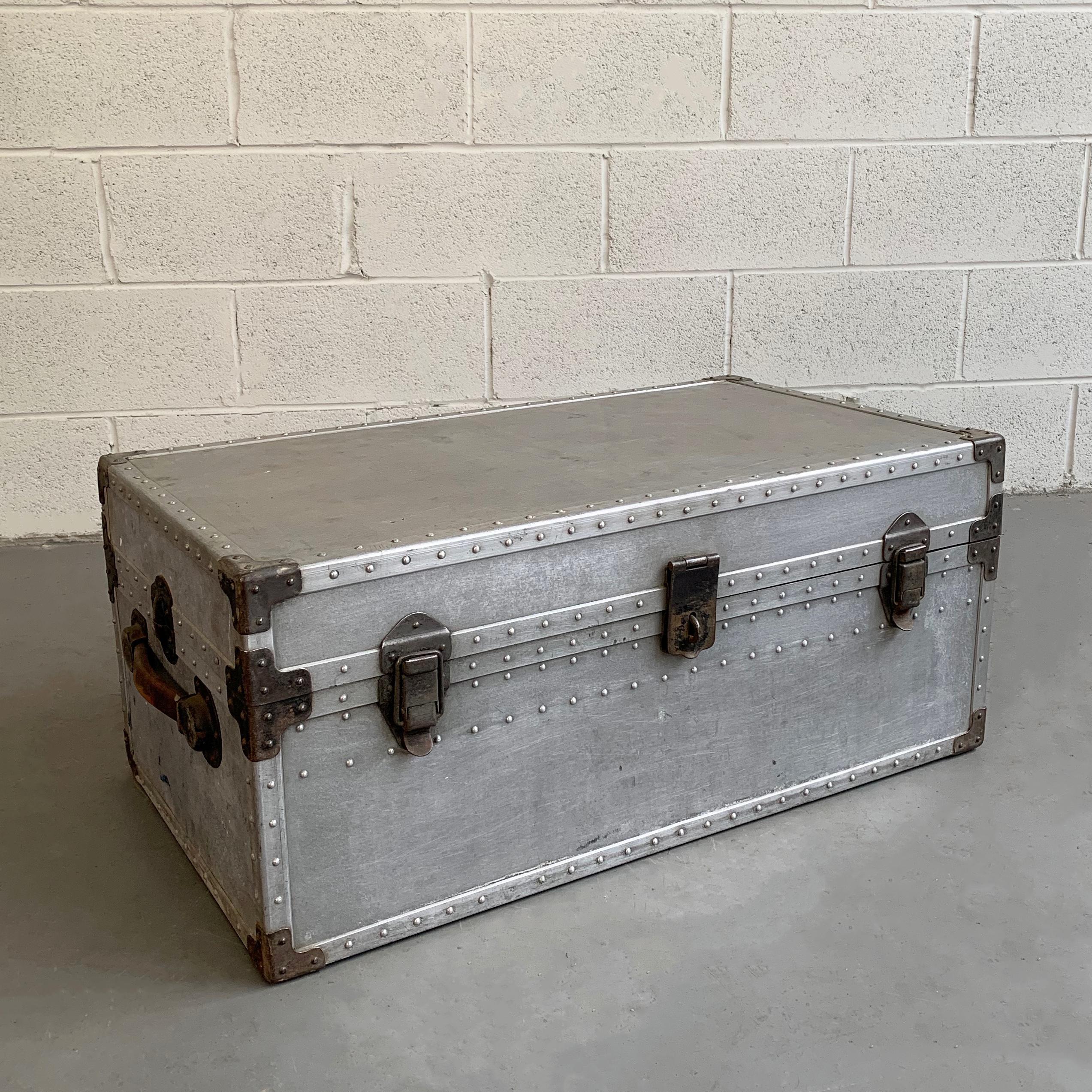 Industrial, aluminum, military trunk features riveted edges, leather handles, and its original green painted interior with tray insert. Two other same size trunks are available with some condition issues.