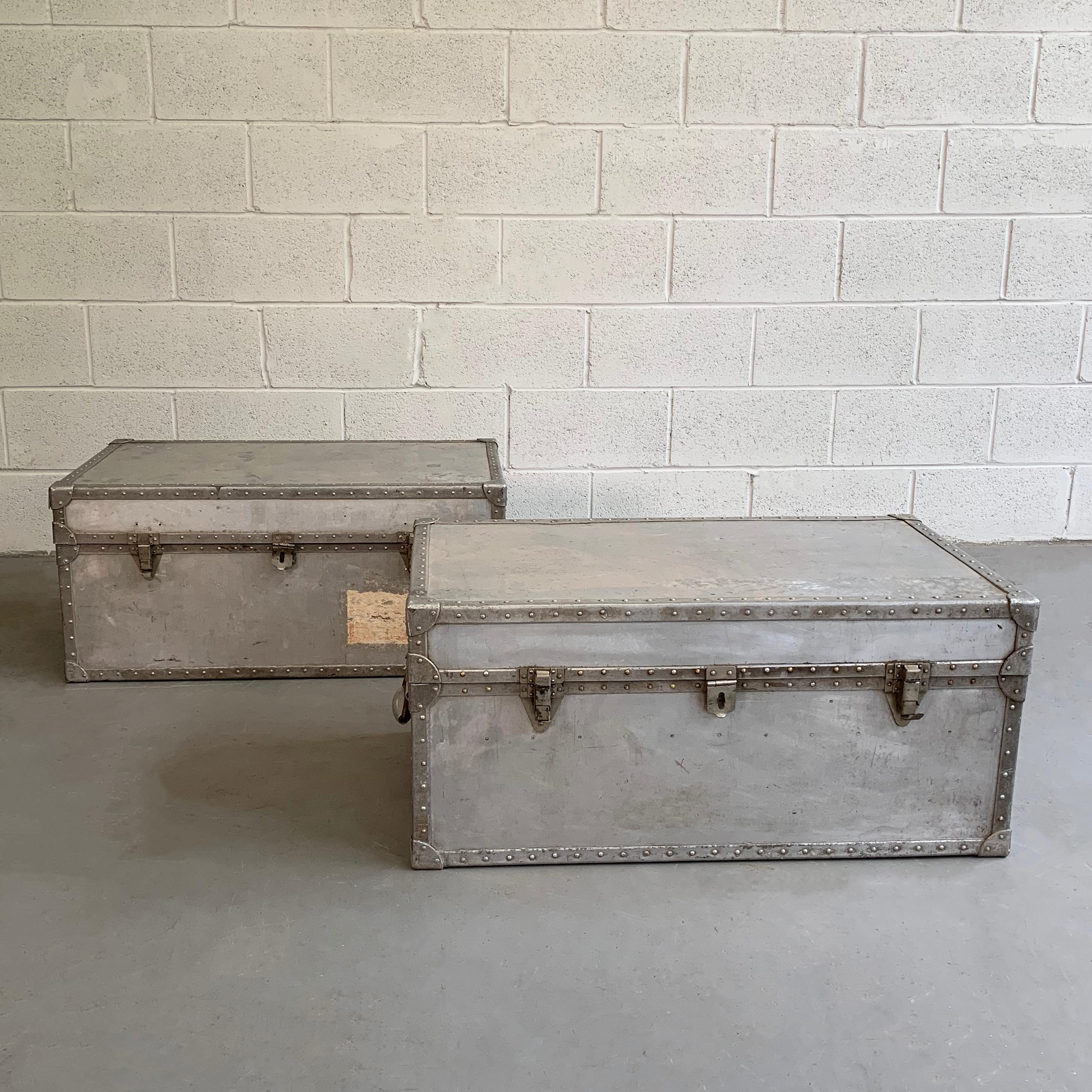 Pair of Industrial, aluminum, military trunks feature riveted edges, aluminum handles and original cargo stamps and stickers. One trunk includes a green tray insert.