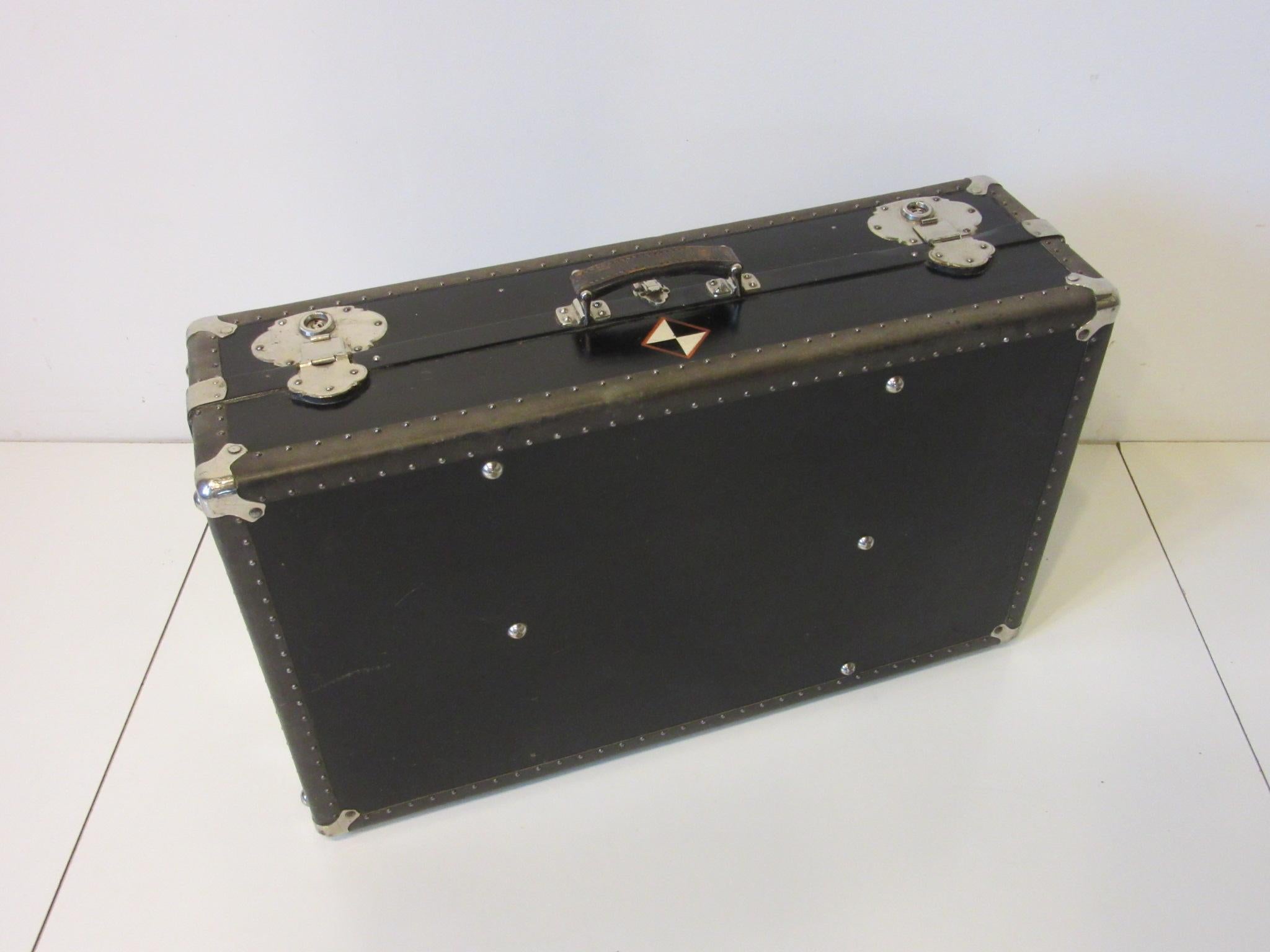 A very well constructed vintage Industrial Art Deco styled trunk suit case having a thick leather handle, banded and small studs to the edging with chromed heavy hardware, locks and corner protectors to the outside. The inside contains a fold away