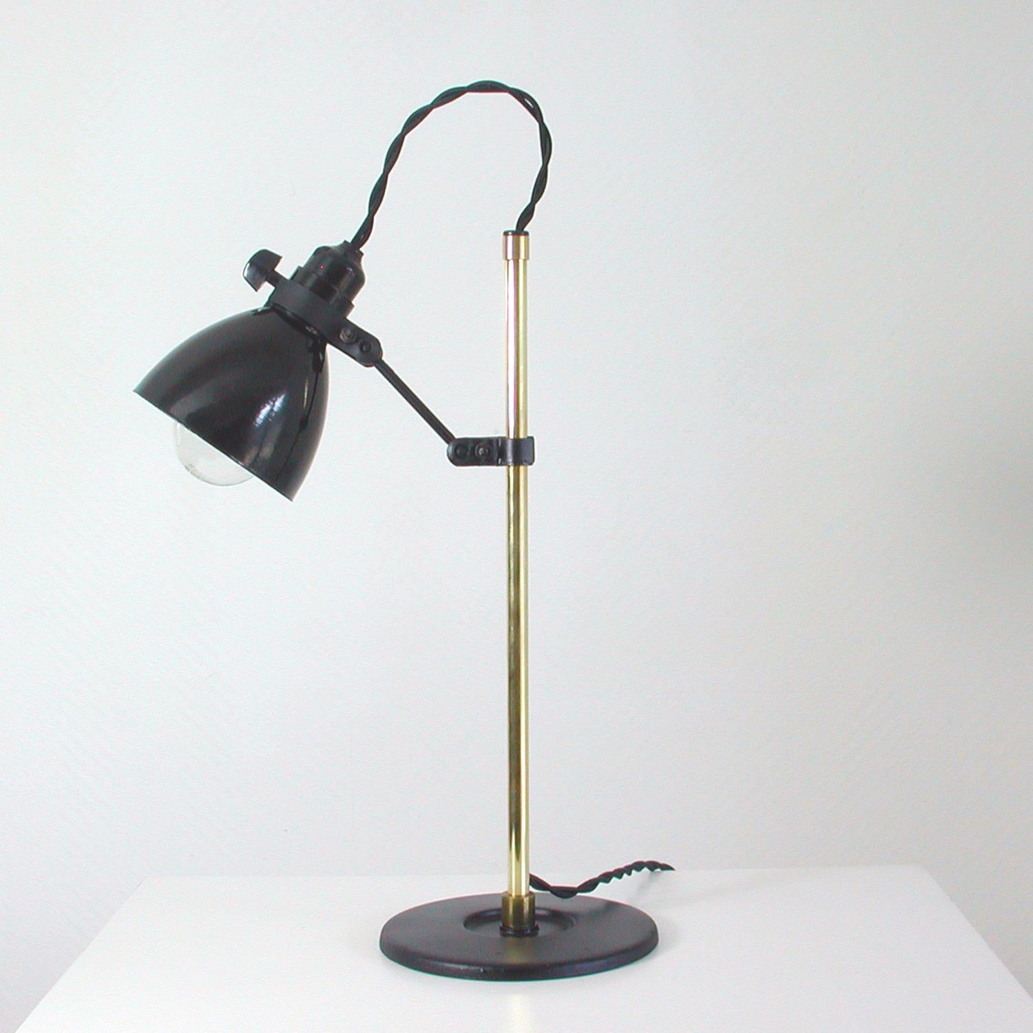 This vintage table lamp was designed and manufactured in Germany in the 1950s. It features a height adjustable bakelite lamp shade, rotatable via multiple joints, a brass lamp arm and black iron base.

The black bakelite shade is shiny and