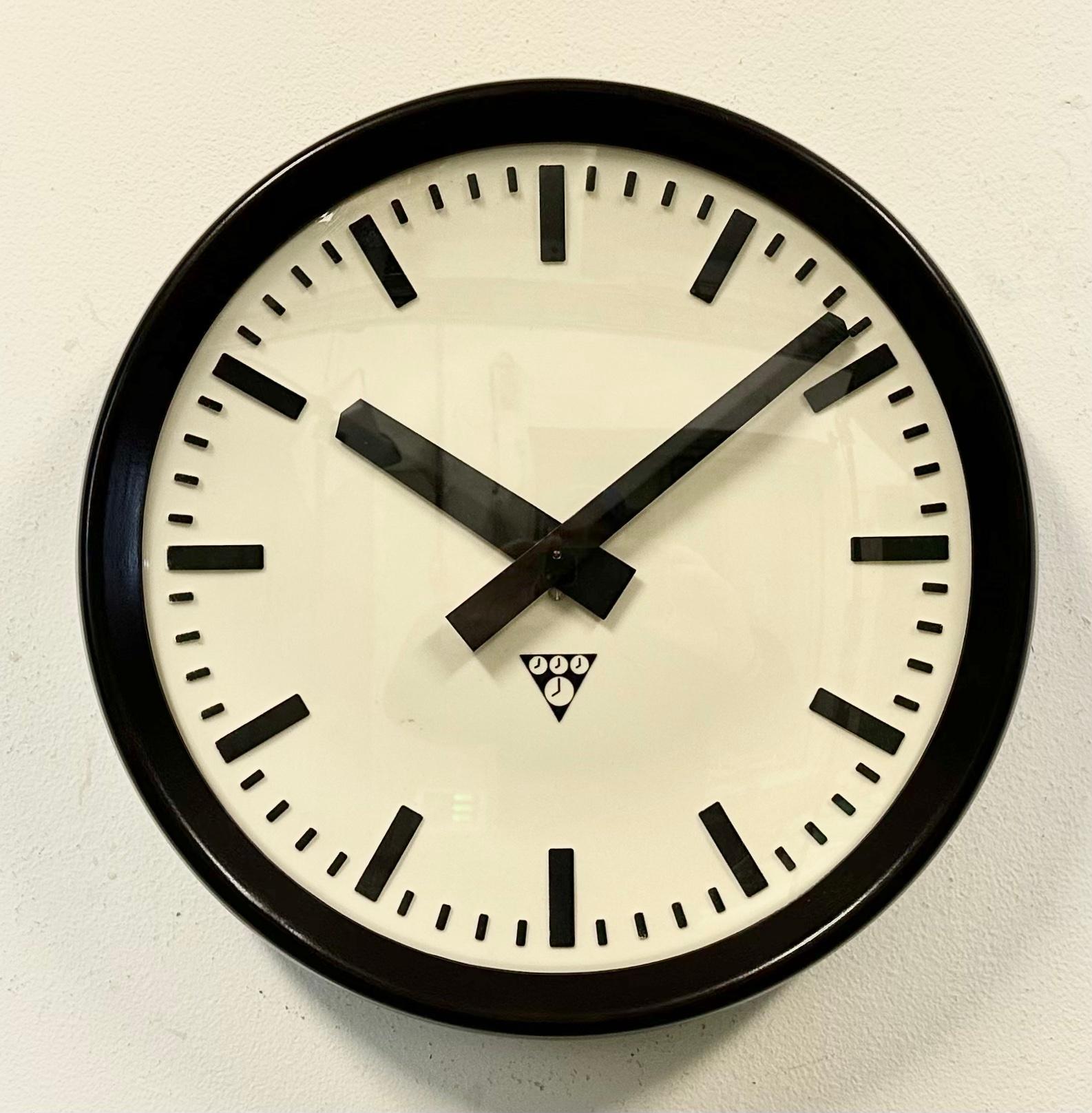 Wall clock produced by Pragotron in former Czechoslovakia during the 1960s. It features a brown bakelite frame, a plastic dial, an aluminium hands and a convex clear glass cover. The piece has been converted into a battery-powered clockwork and