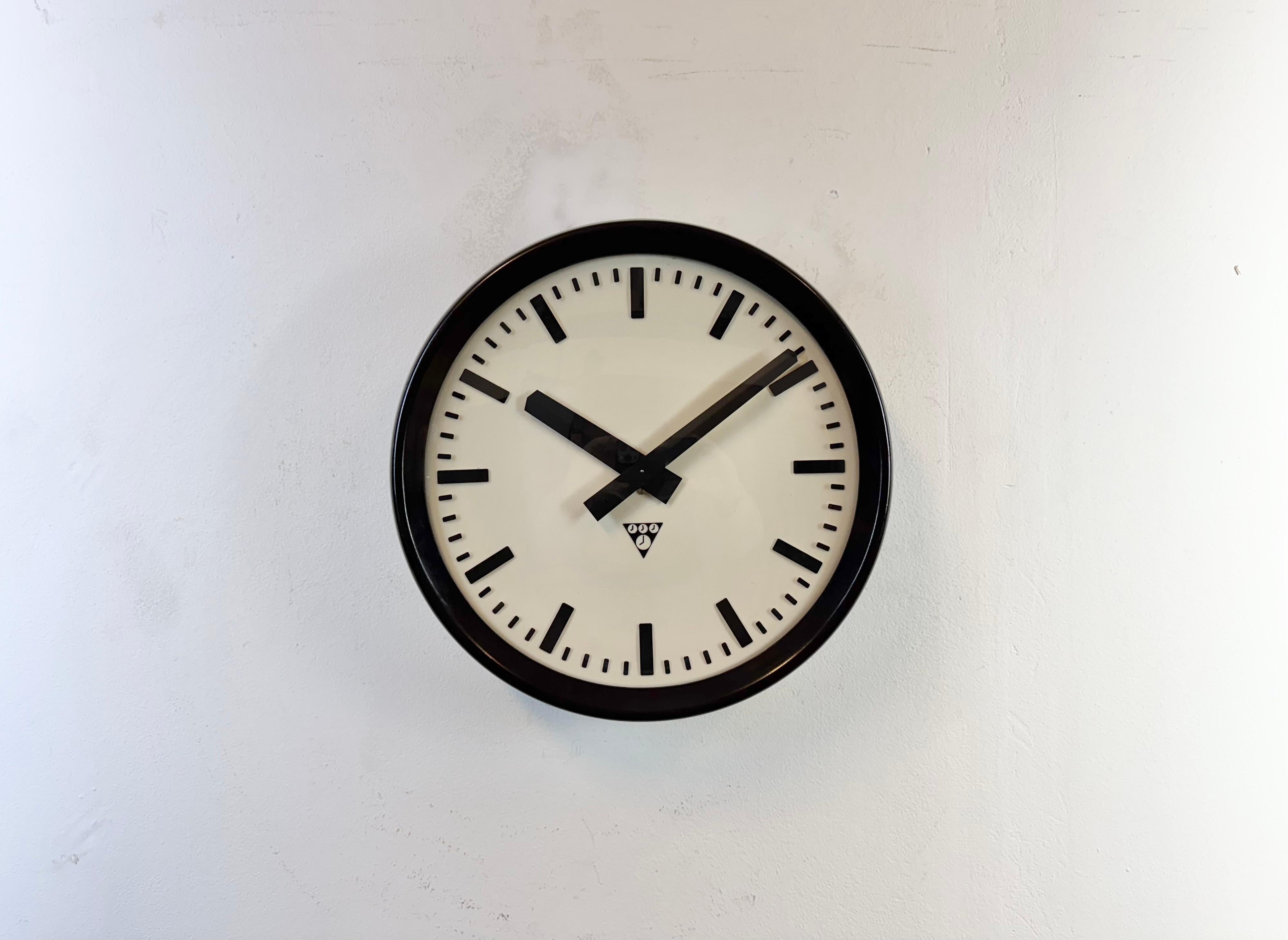 Este reloj de pared fue fabricado por Pragotron en la antigua Checoslovaquia durante la década de 1960. Presenta un marco y un fondo de baquelita marrón, una esfera de plástico, unas agujas de aluminio y un  Cubierta convexa de cristal transparente.