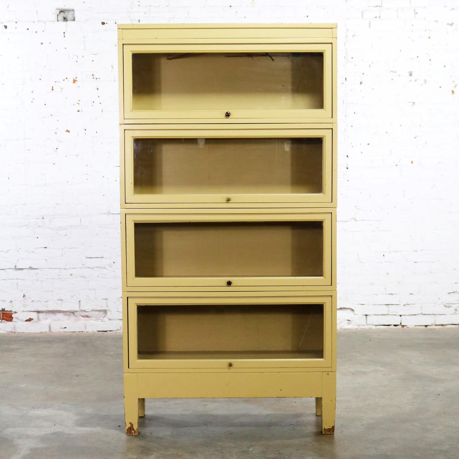 Handsome vintage Globe Wernicke Industrial stacking barrister bookcase with a distressed golden yellow painted finish to the wood cases and wood framed glass doors. There are four separate cases, a top, and a bottom. They are in wonderful vintage